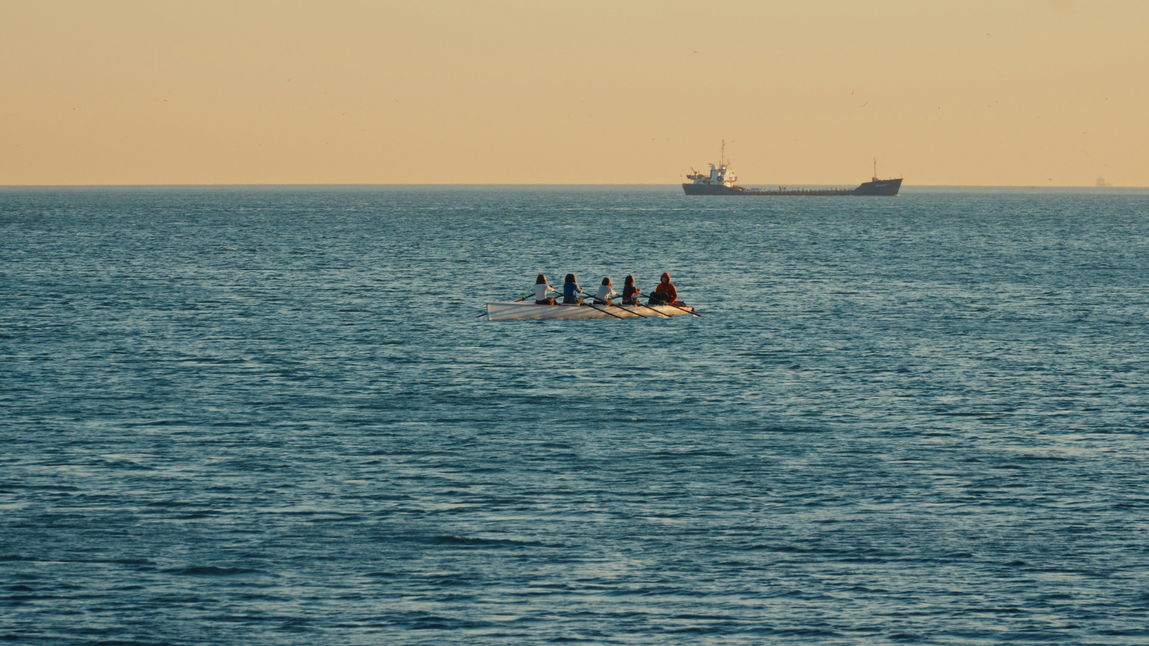 People in a small boat on the ocean with ship