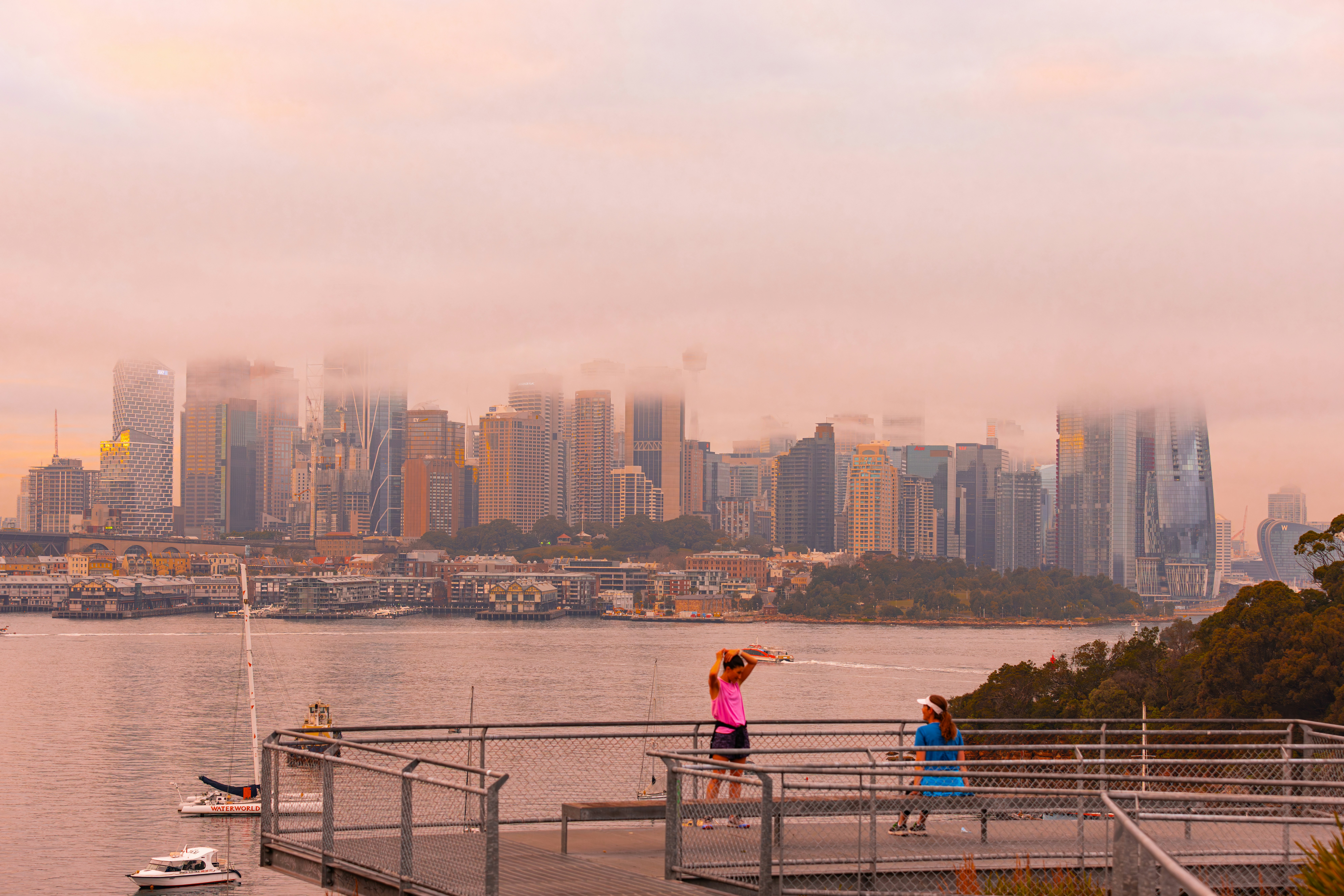 Two women on a pier overlooking a foggy city skyline