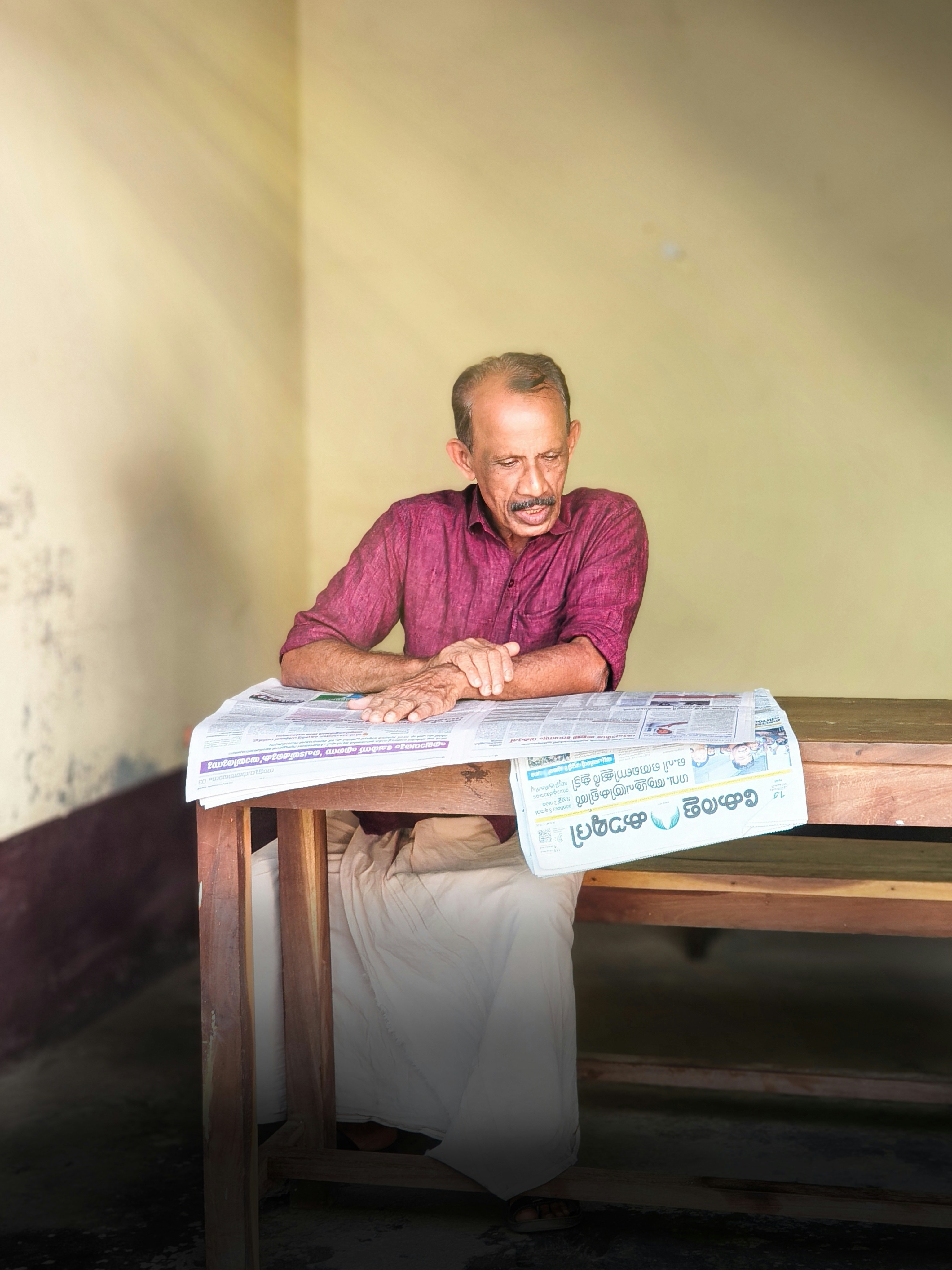 Man in maroon shirt reading newspaper at table