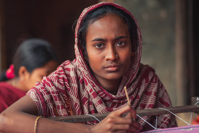 A young Bangladeshi woman in a headscarf working at a textile loom