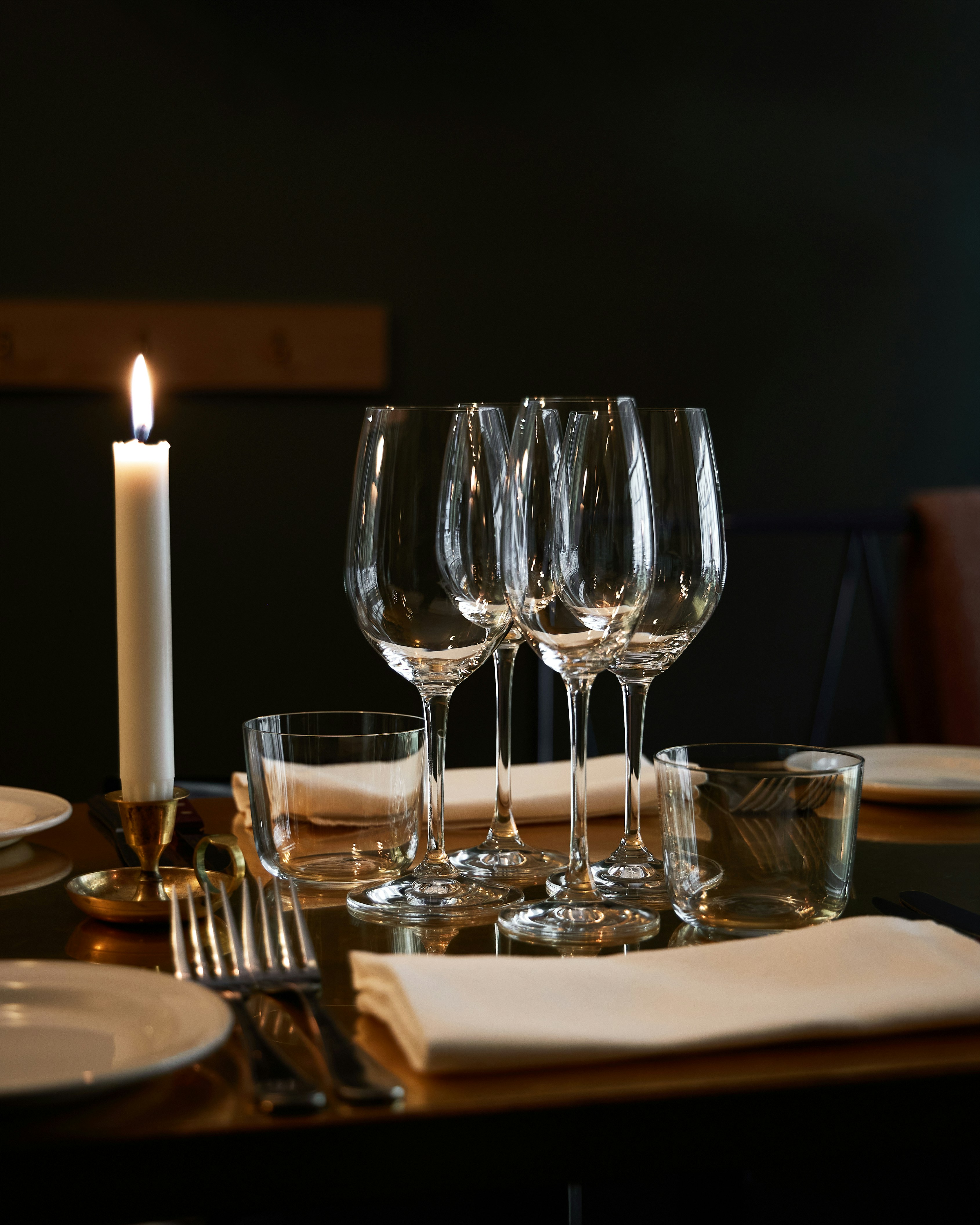 Una vela encendida y copas de vino vacías sobre una mesa.