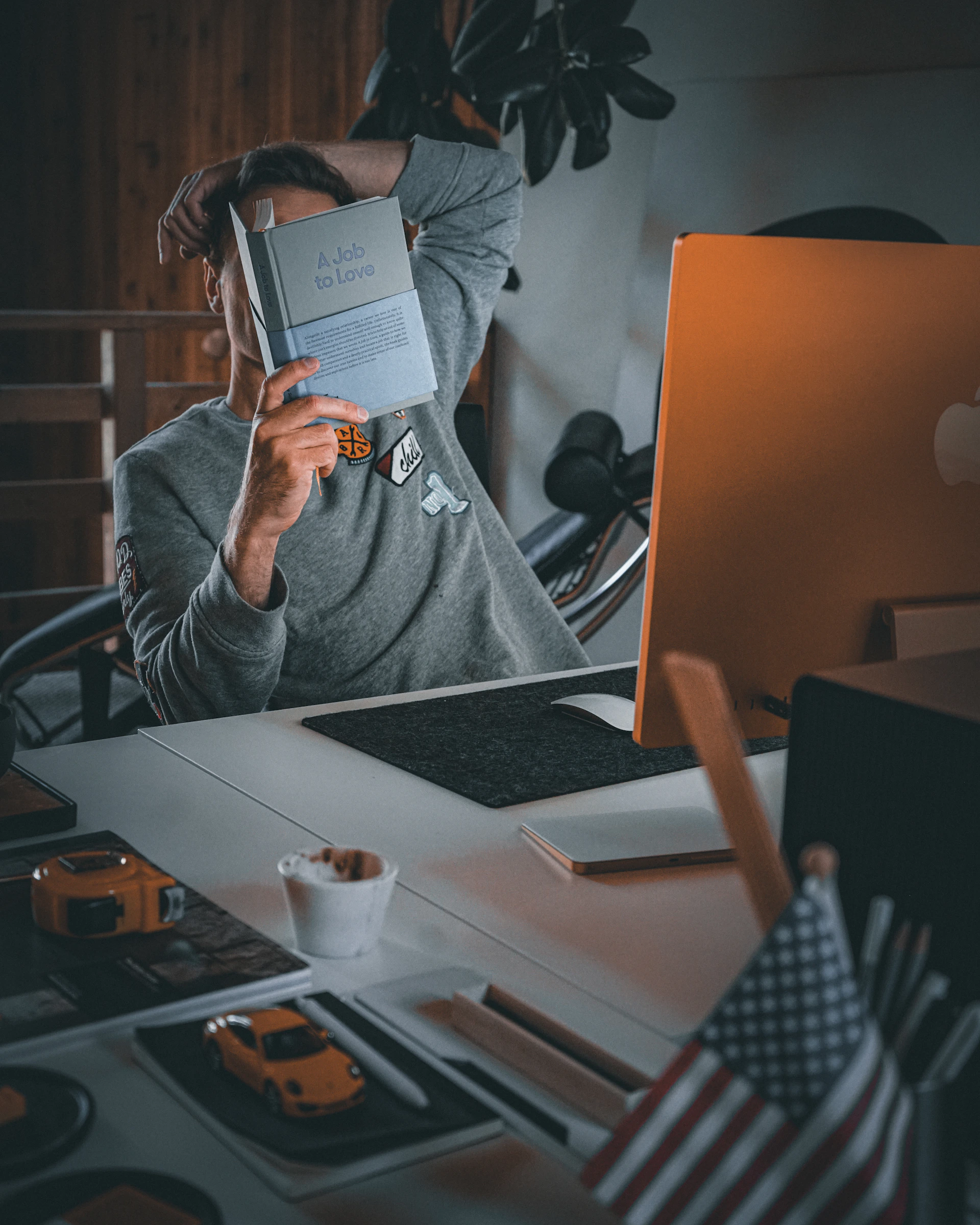 Person reading a book at a desk with computer.