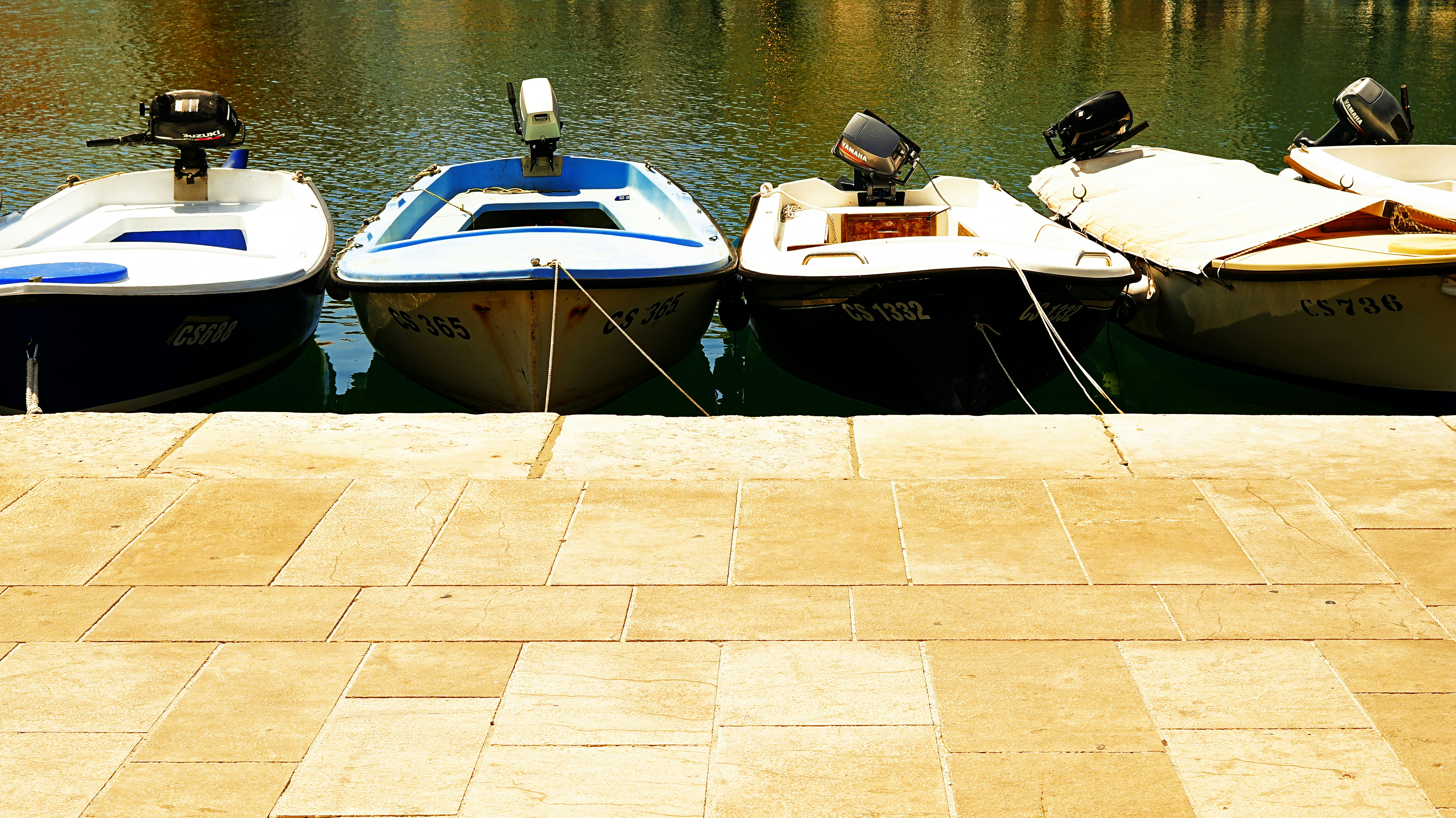 Quatre petites embarcations amarrées par une passerelle en pierre.