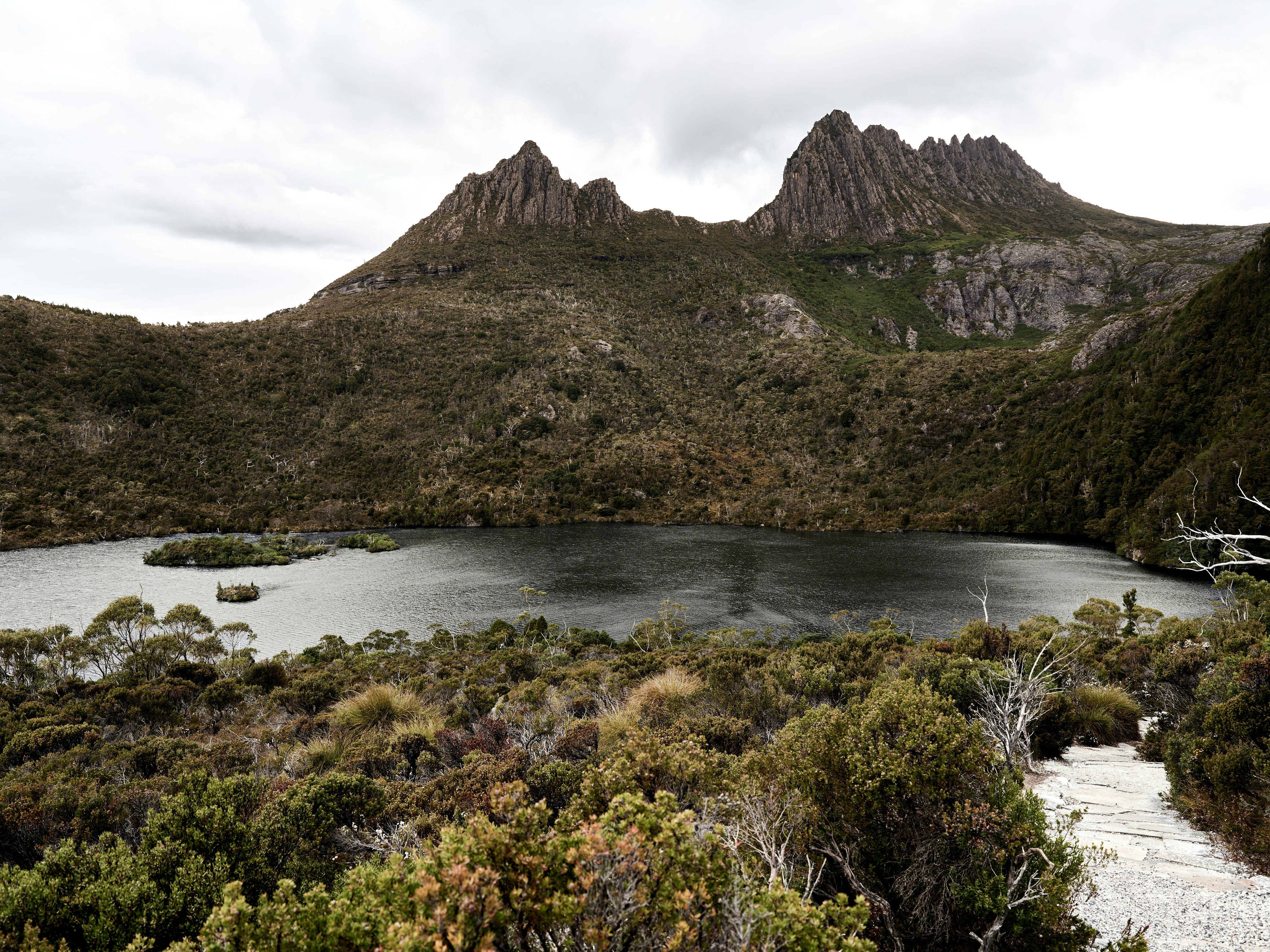 Mountain peaks reflect in a dark lake surrounded by vegetation.
