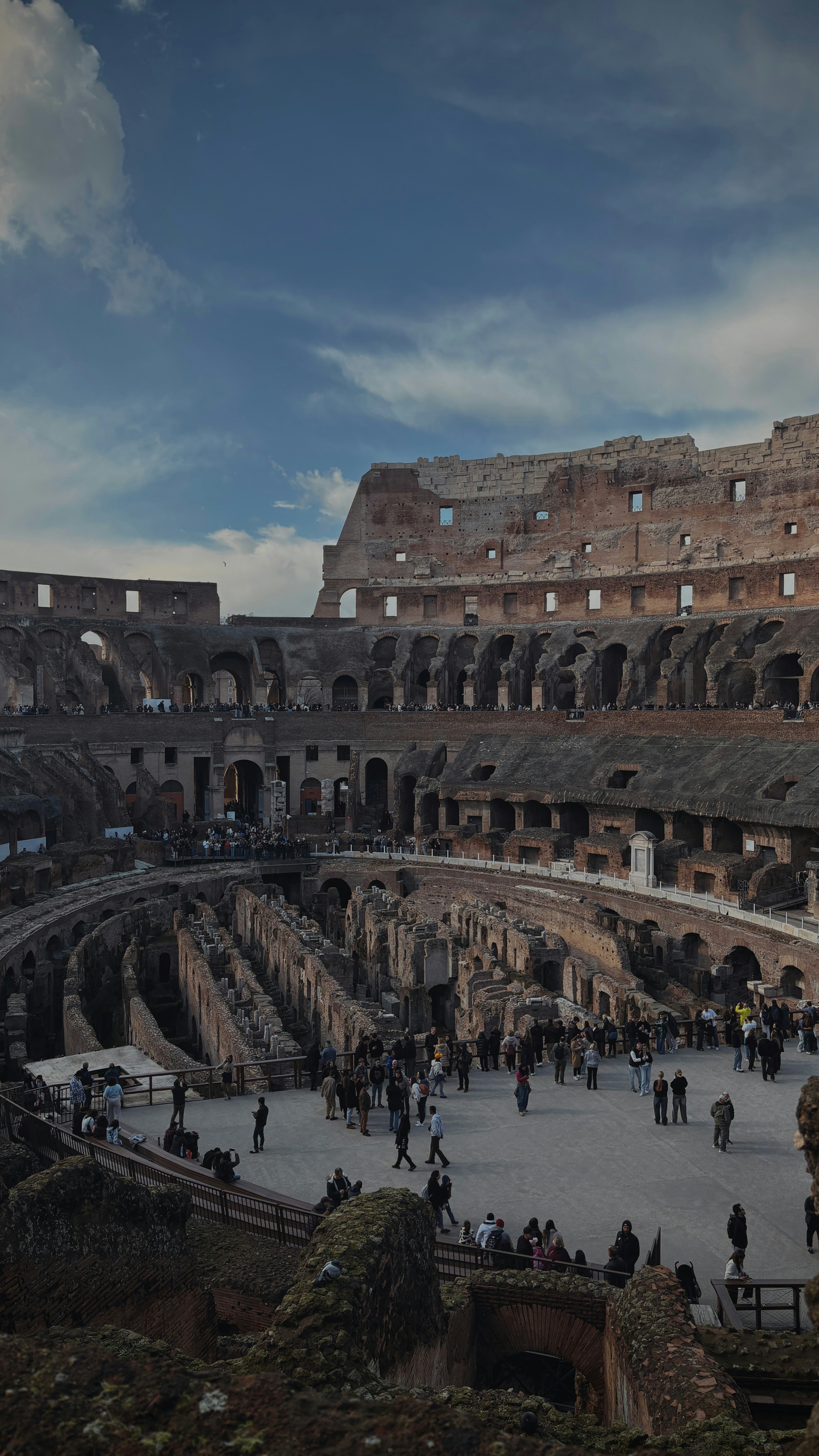 Interni del Colosseo con turisti sotto un cielo azzurro nuvoloso