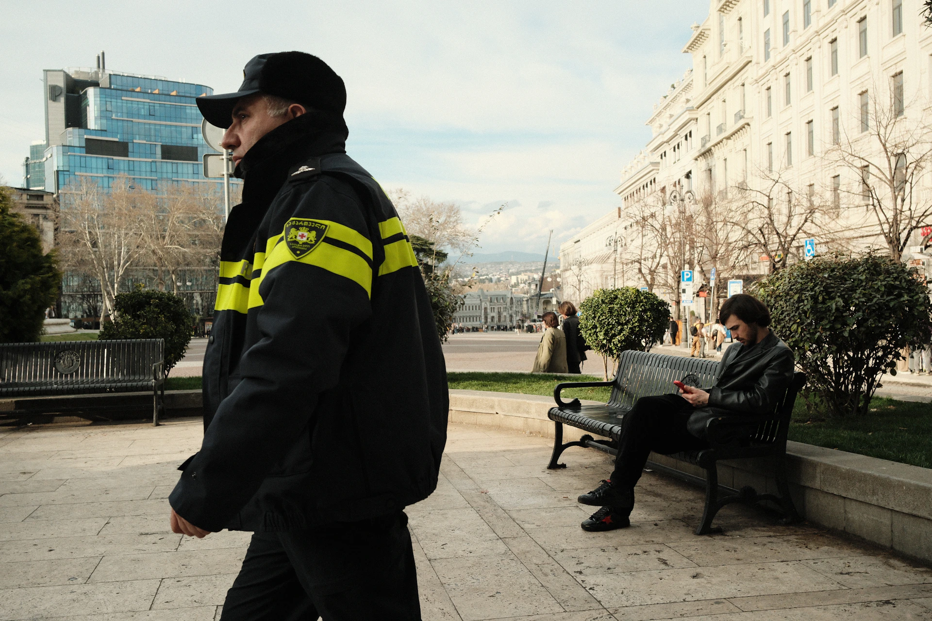 Man in uniform walks past man on park bench.