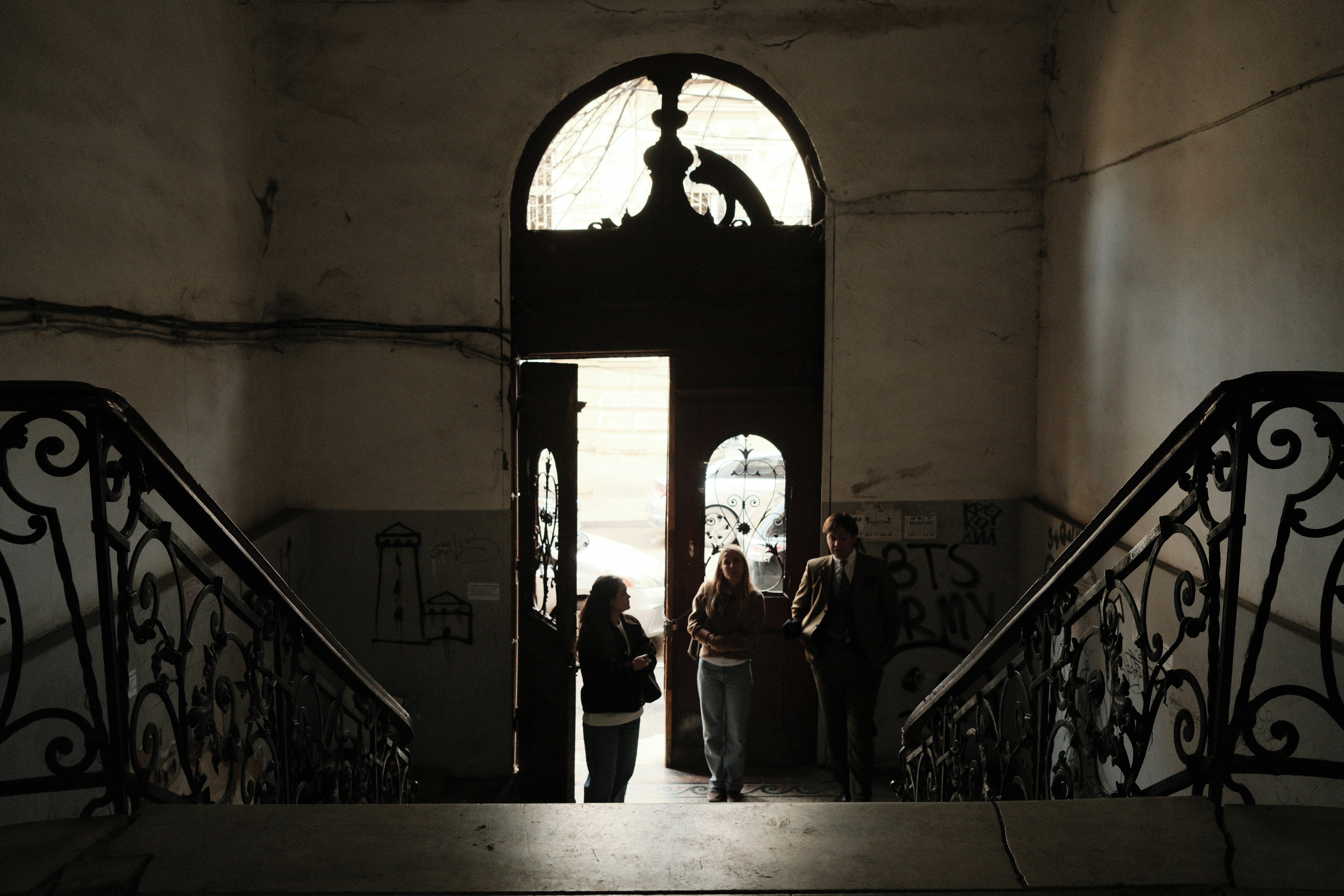 Silhouetted figures stand near an open doorway with stairs.