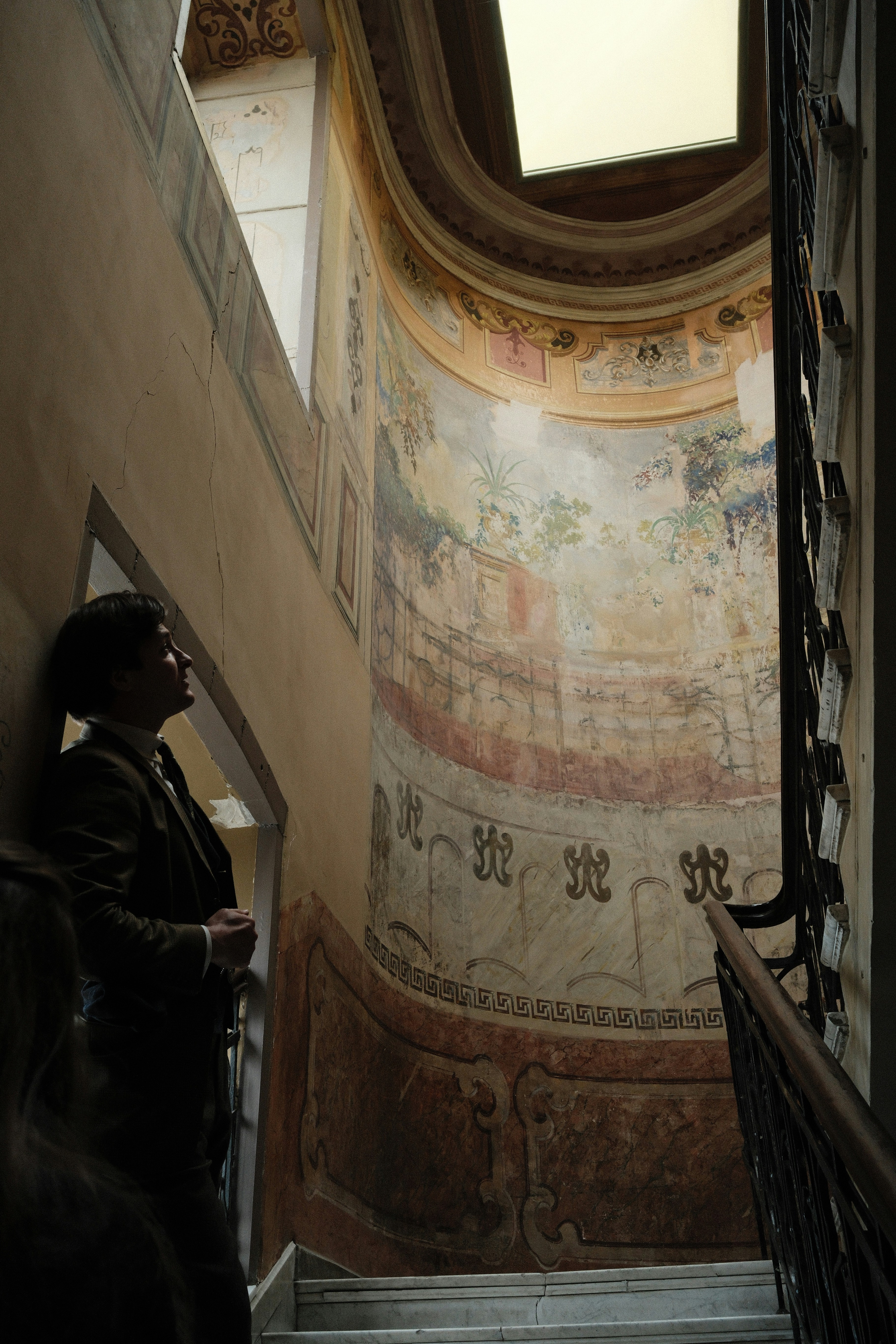 Man in suit looking up at ornate mural on staircase