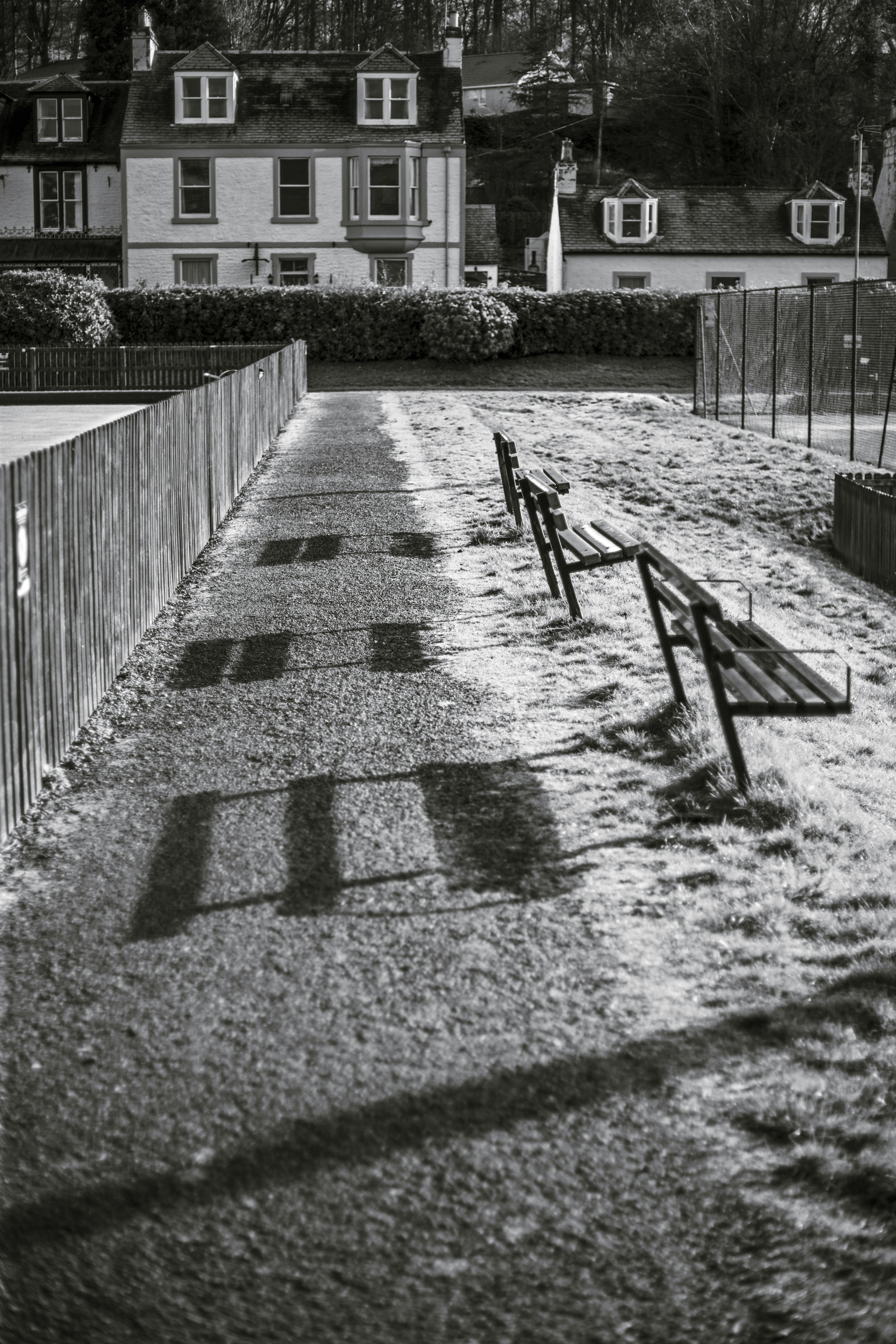 Shadows of benches on a grassy path with houses behind.