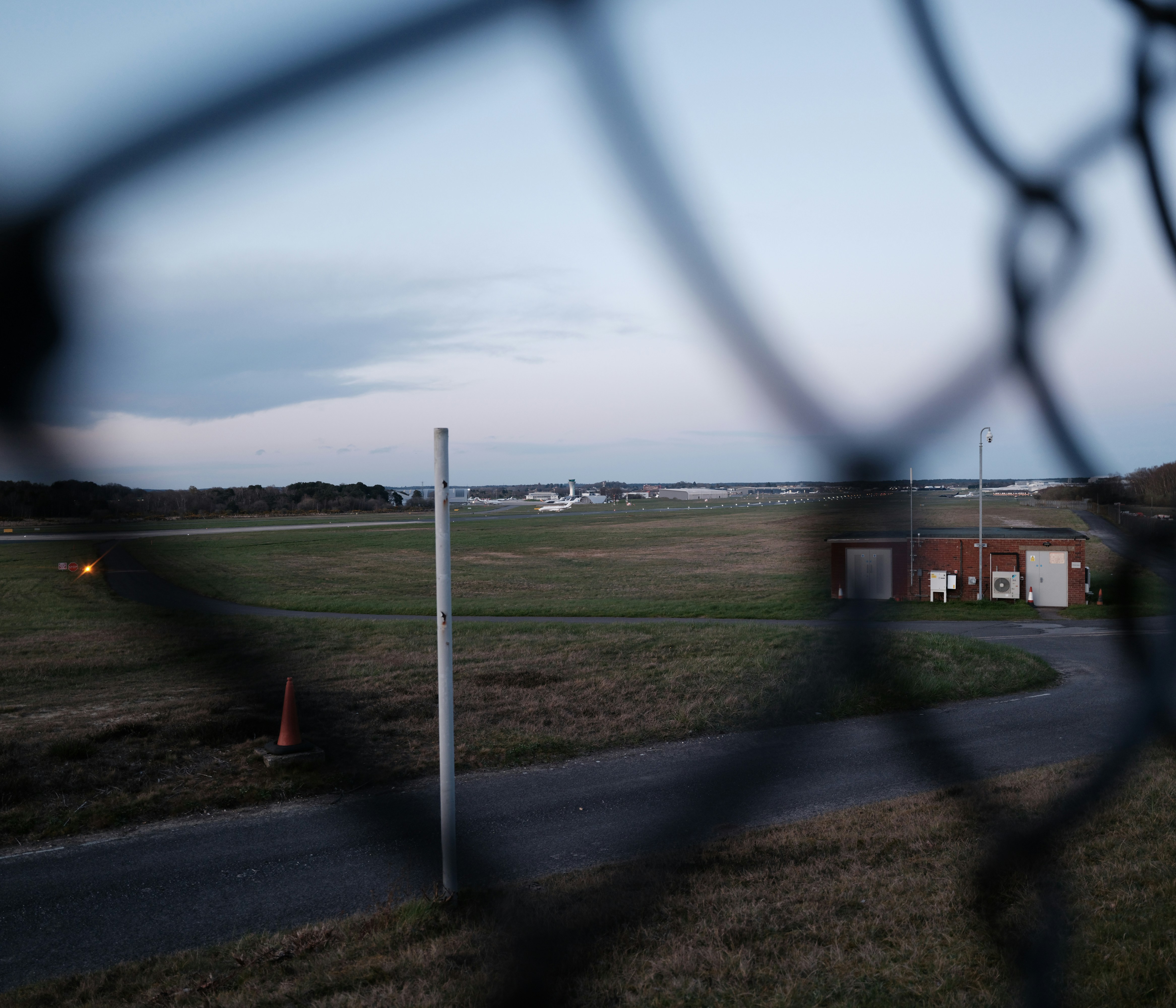 Airport tarmac with distant airplane seen through fence.