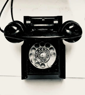 A vintage black rotary dial telephone on a white surface.