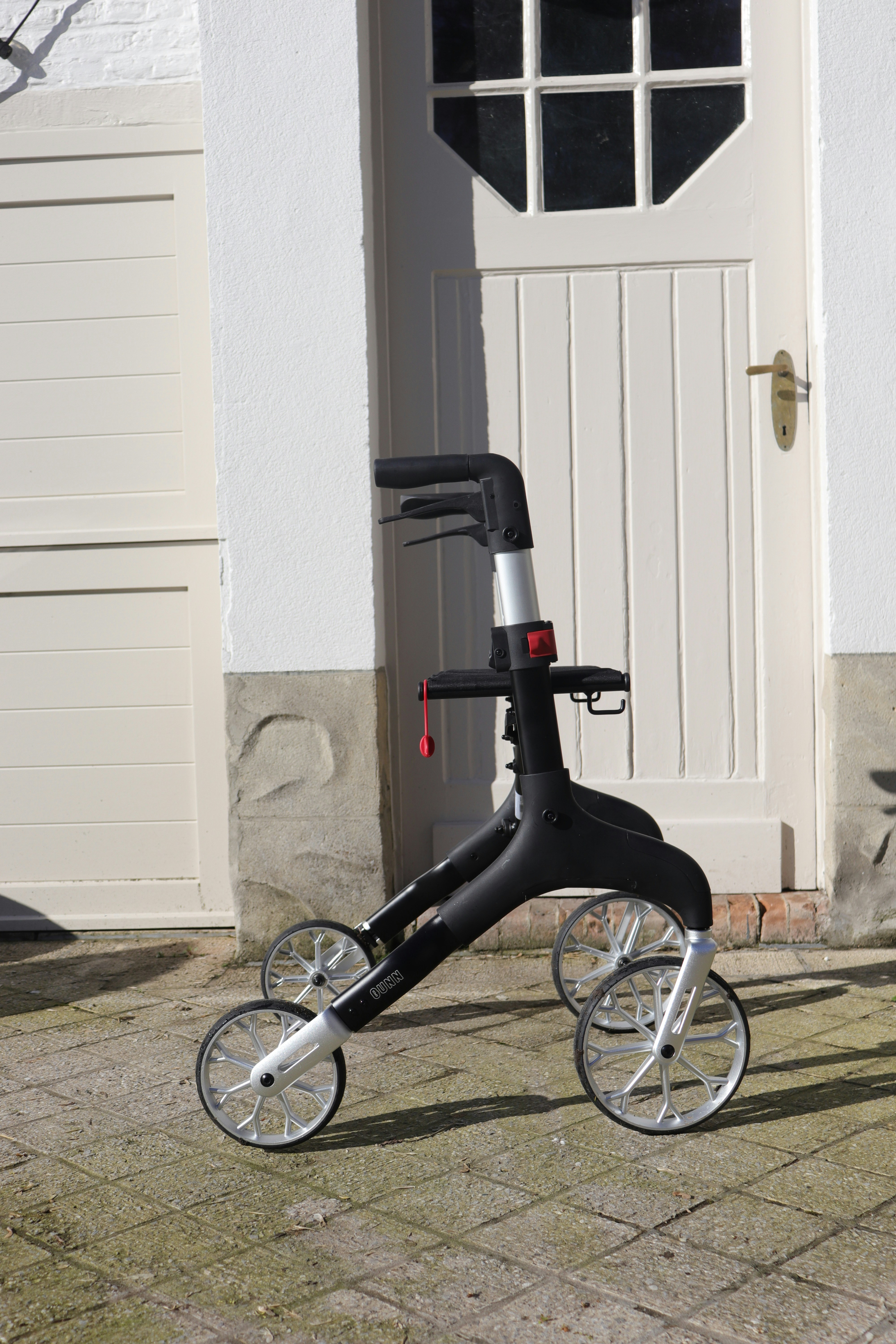 A black and silver four-wheeled walker stands on pavement.