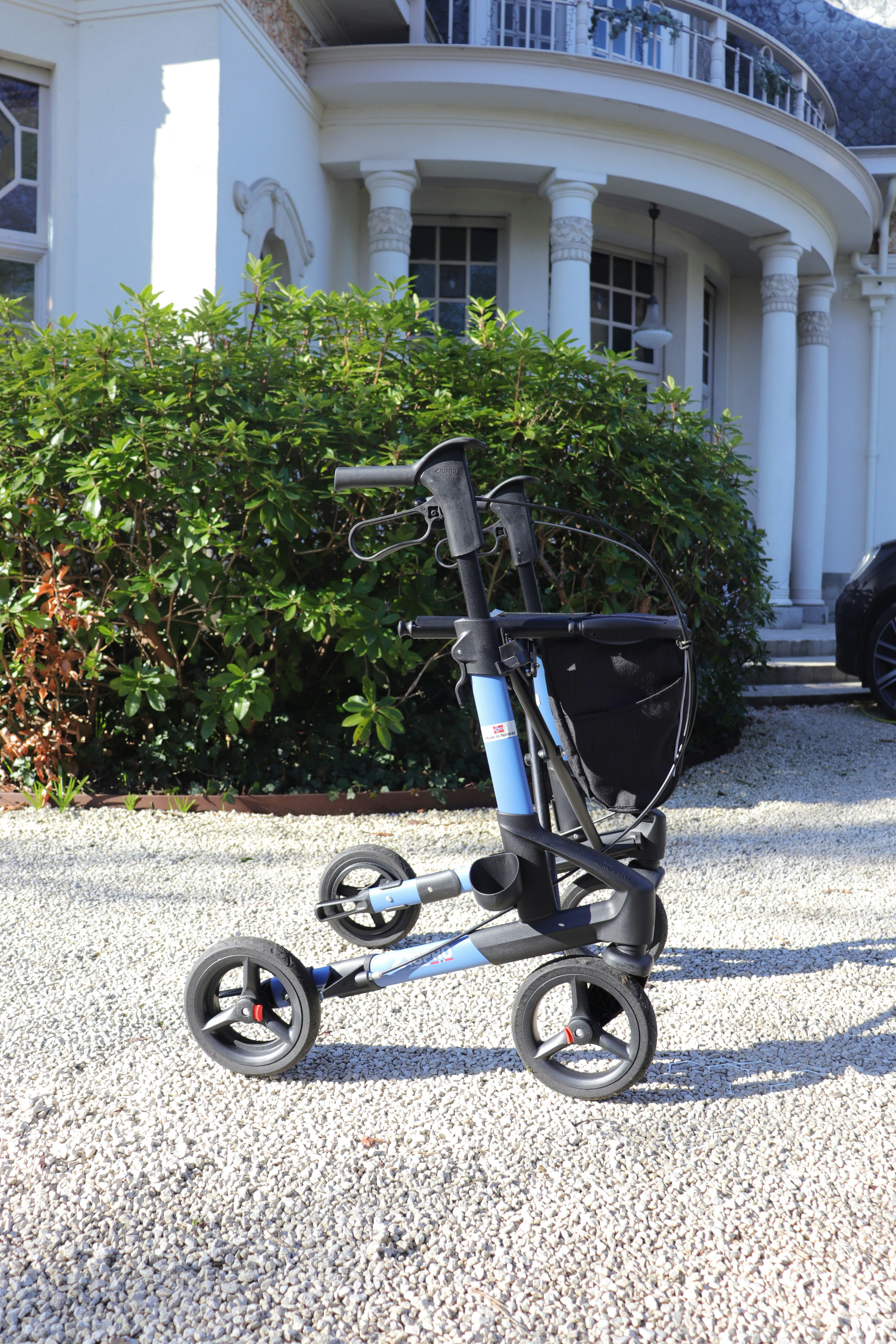 A blue walker with four wheels on gravel.