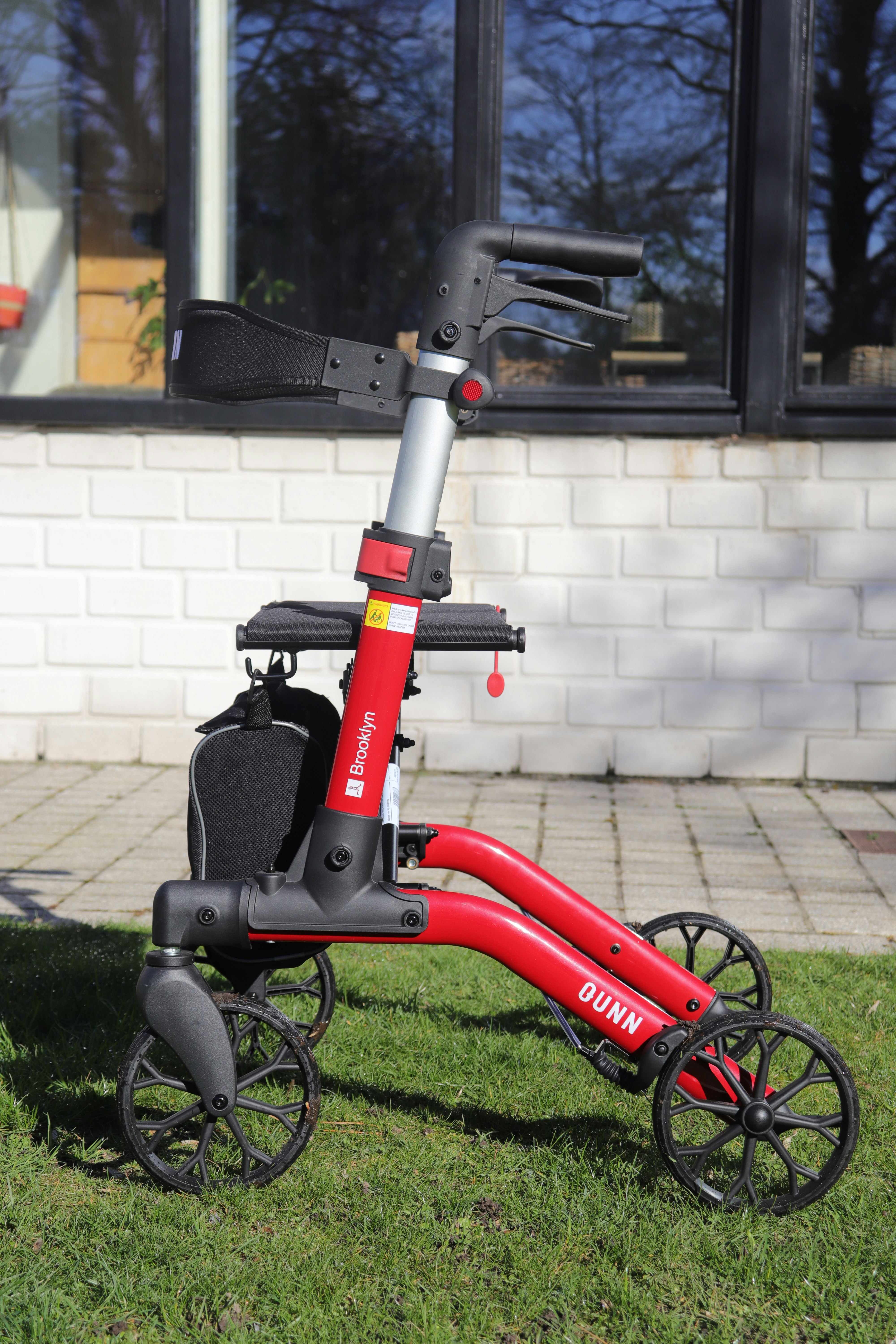 A red walker with four wheels on grass.