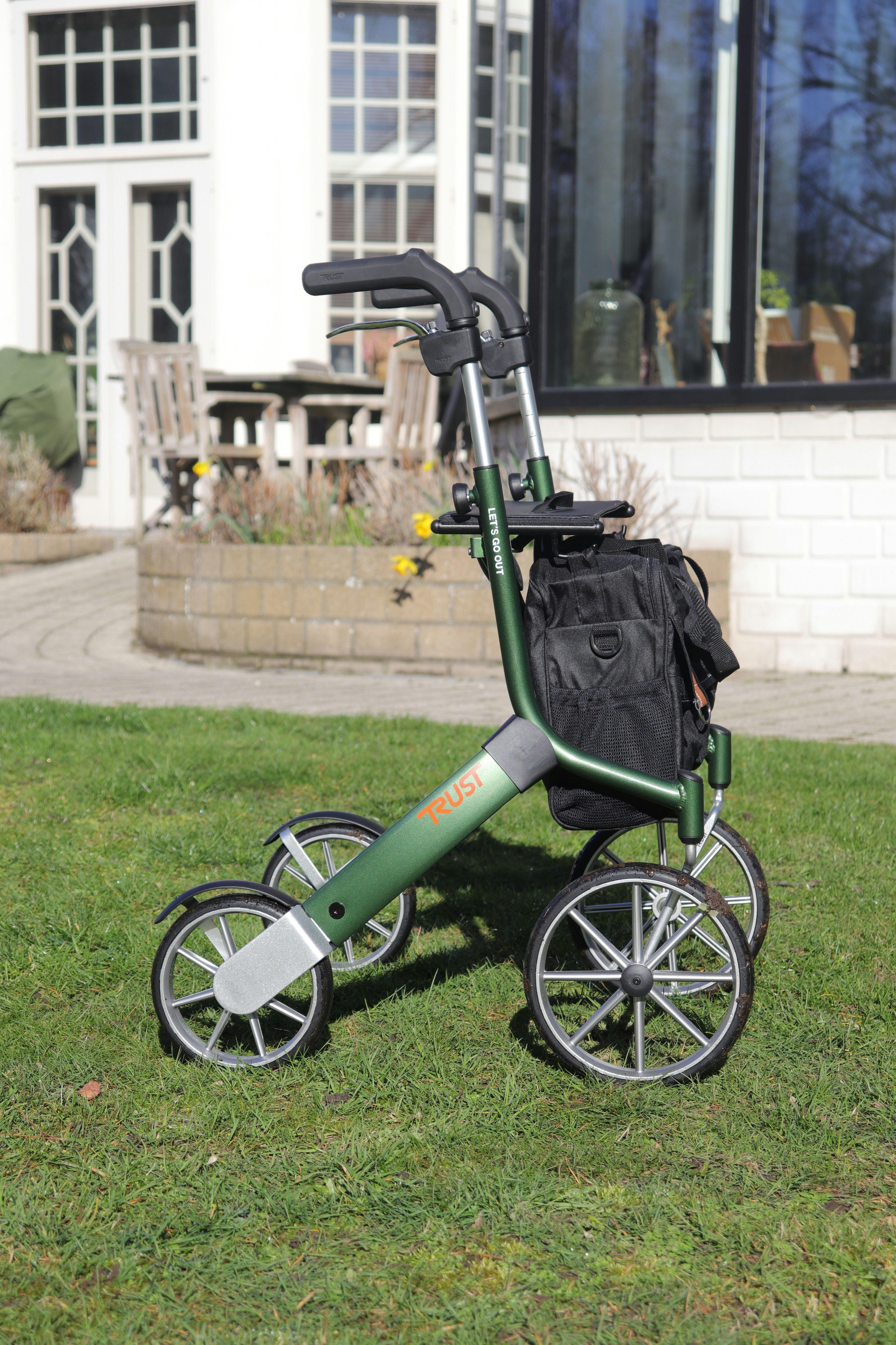 A green four-wheeled walker with a black bag.
