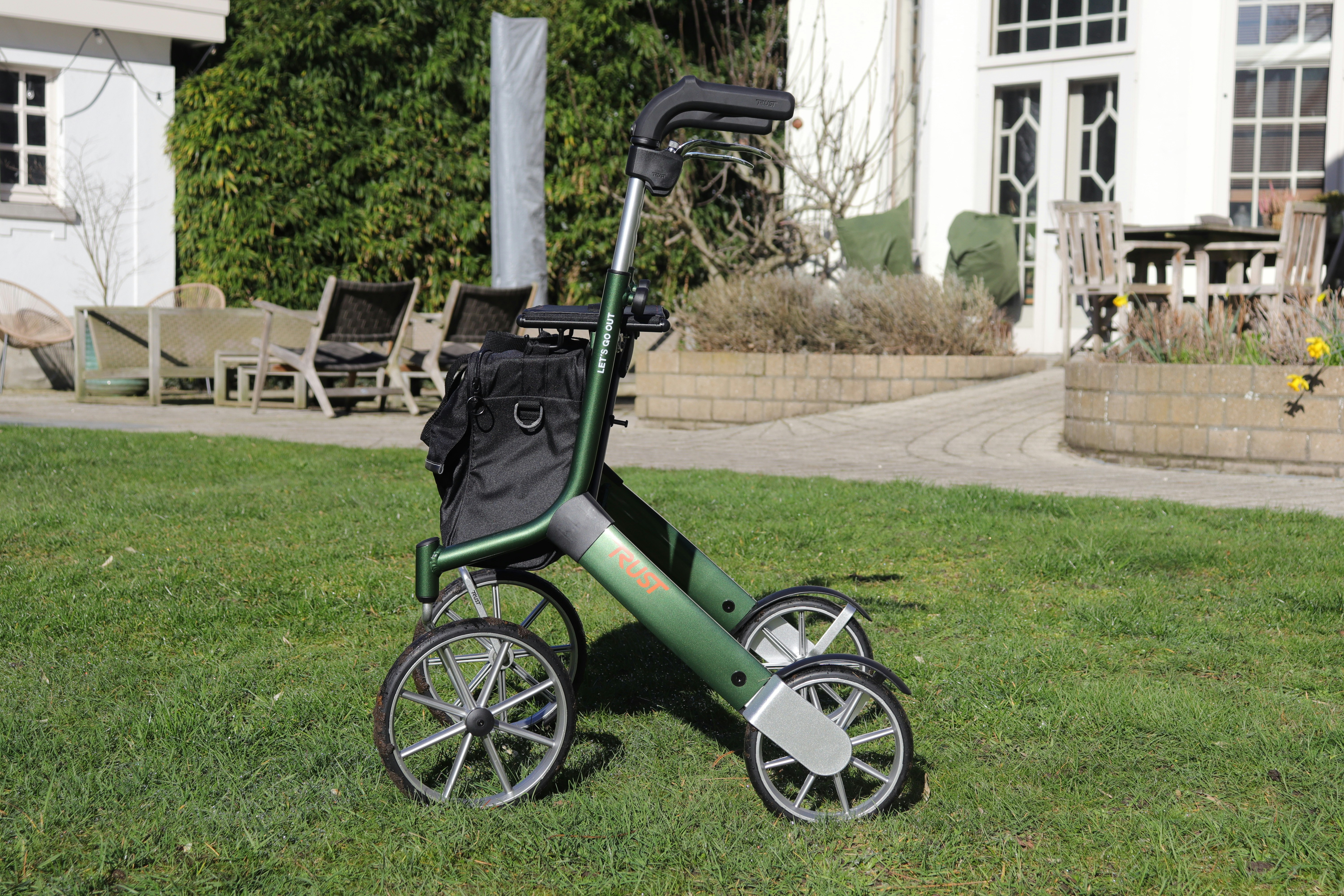 A green walker with four wheels on grass.