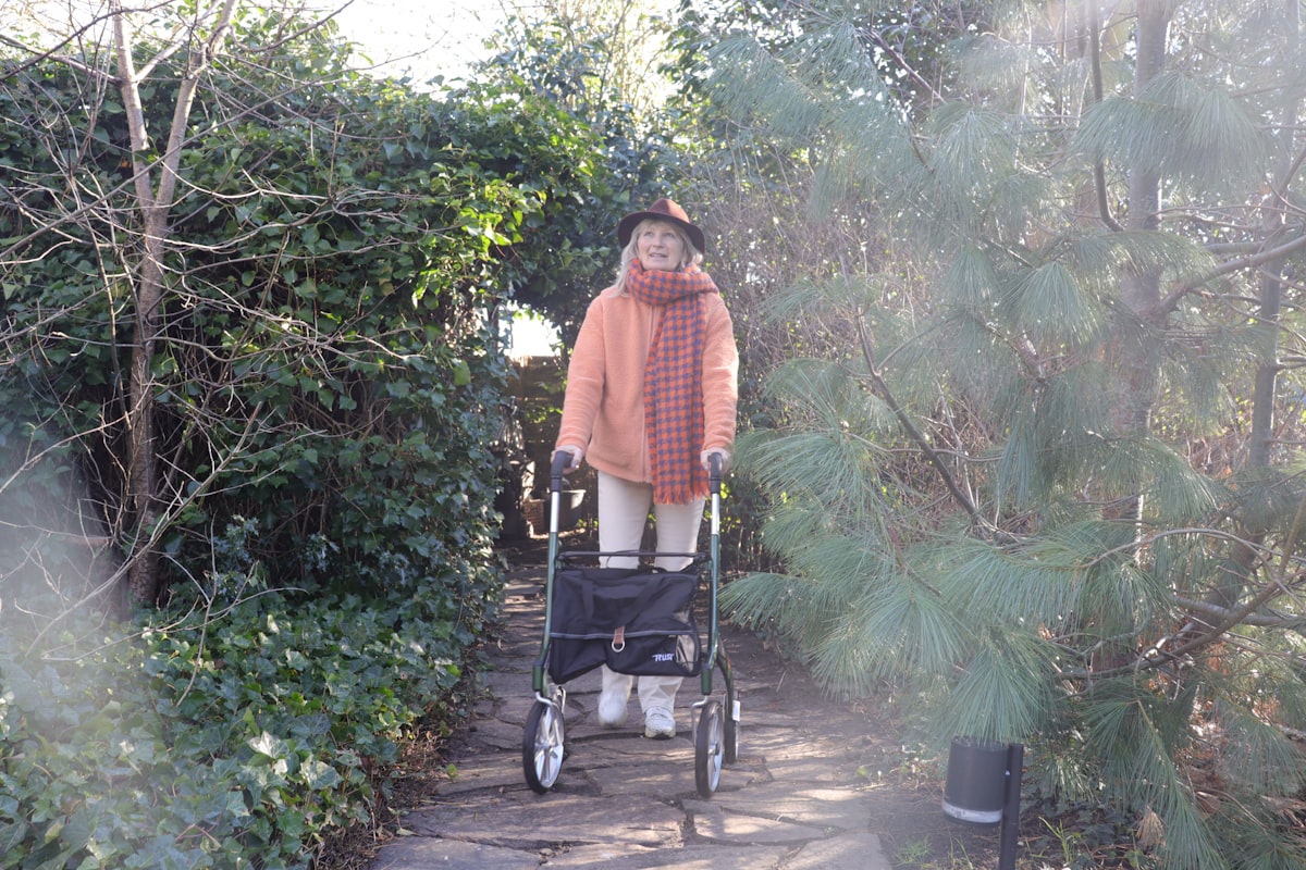 An elderly woman with a walker on a garden path