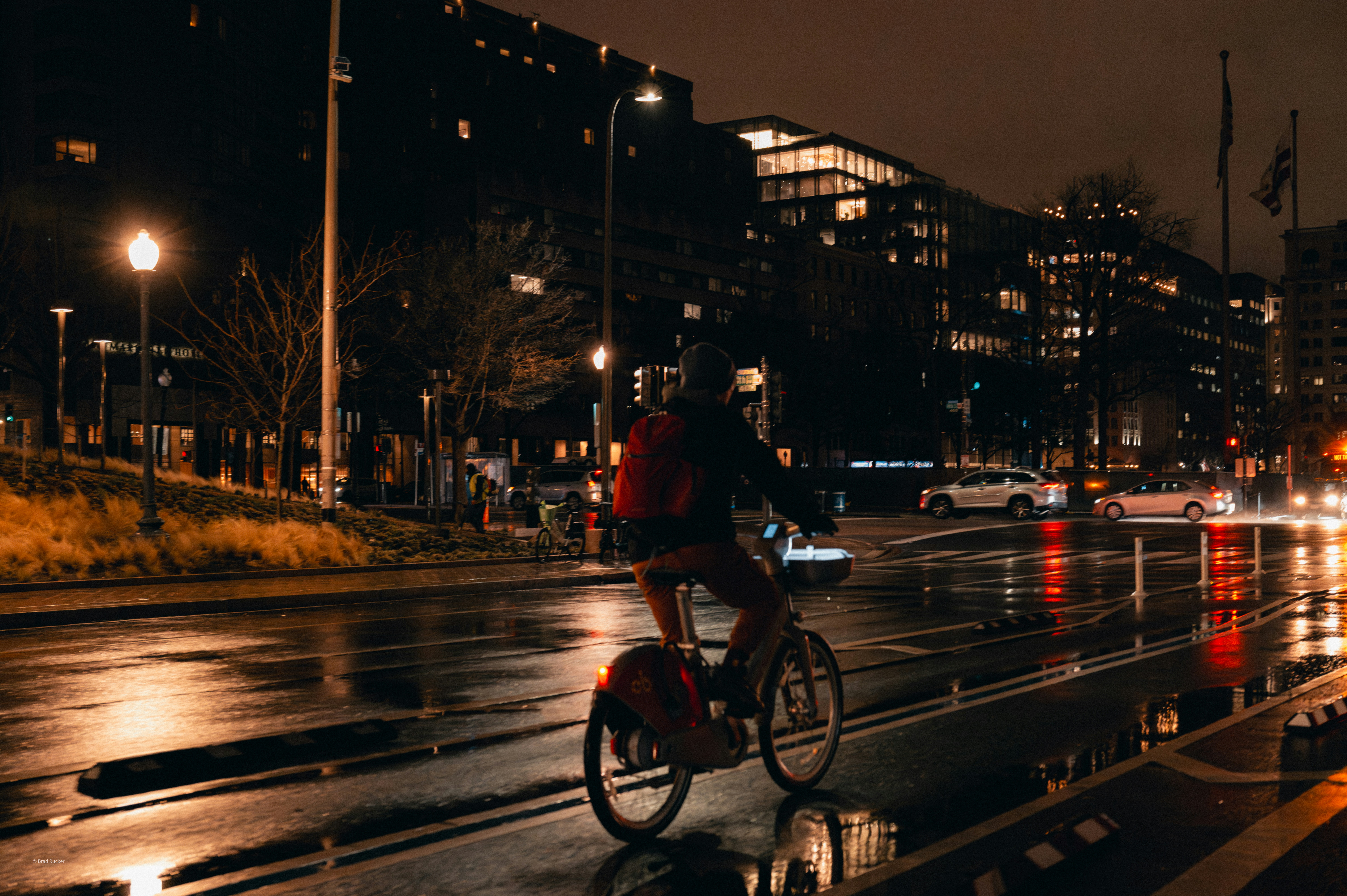Cyclist rides on wet city street at night.