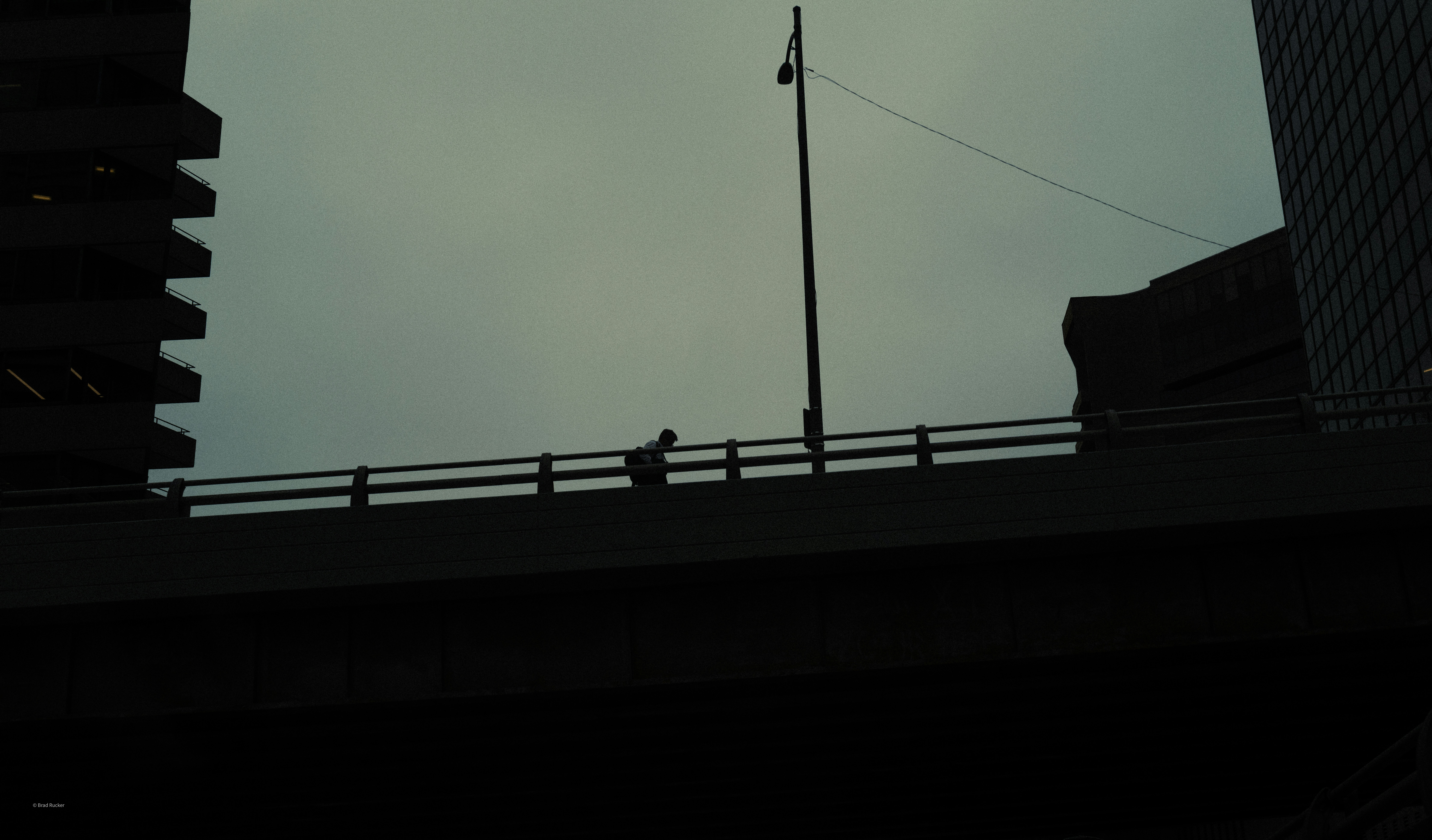 A lone figure walks across a bridge at dusk.
