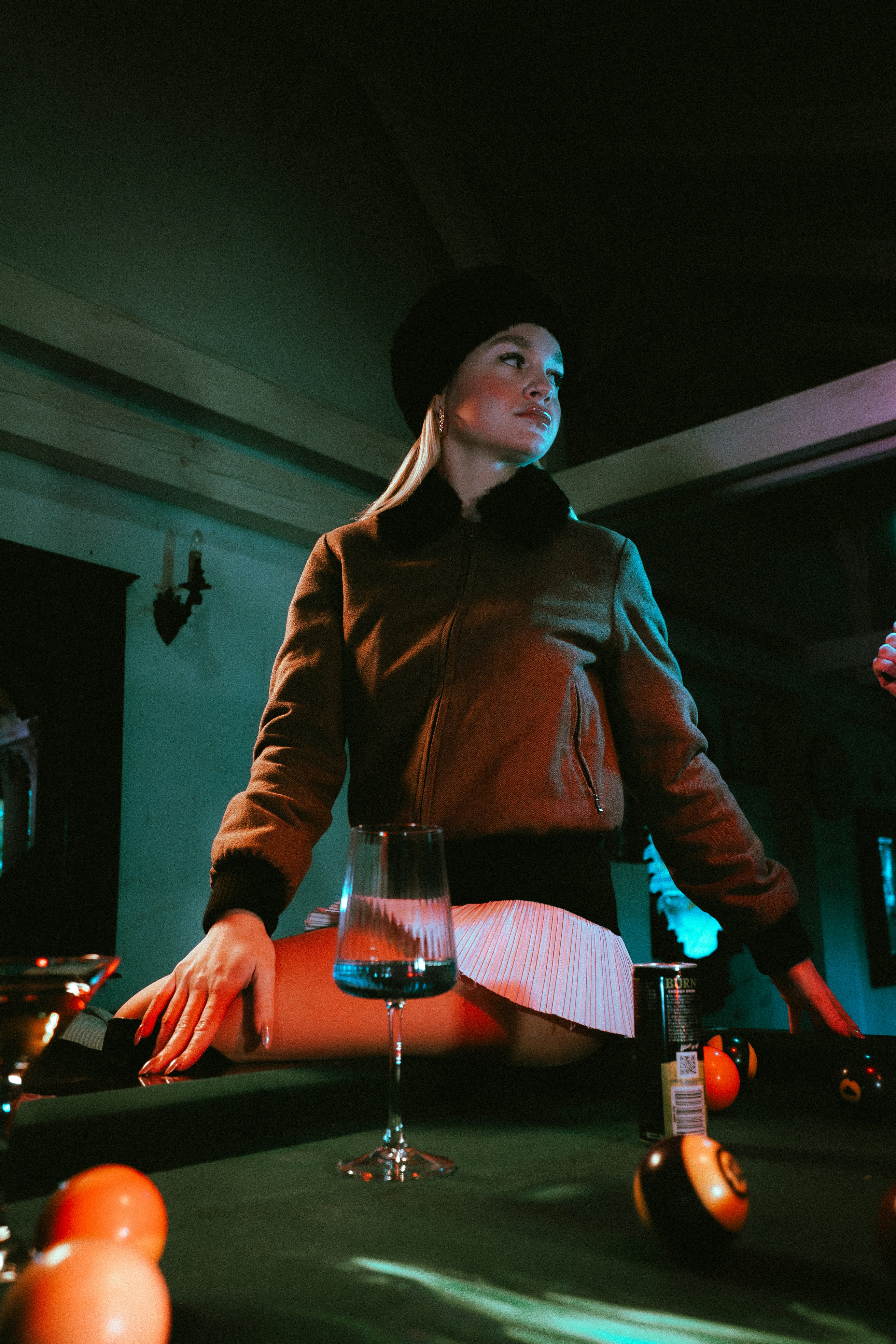 Woman in jacket sits on a pool table with balls.