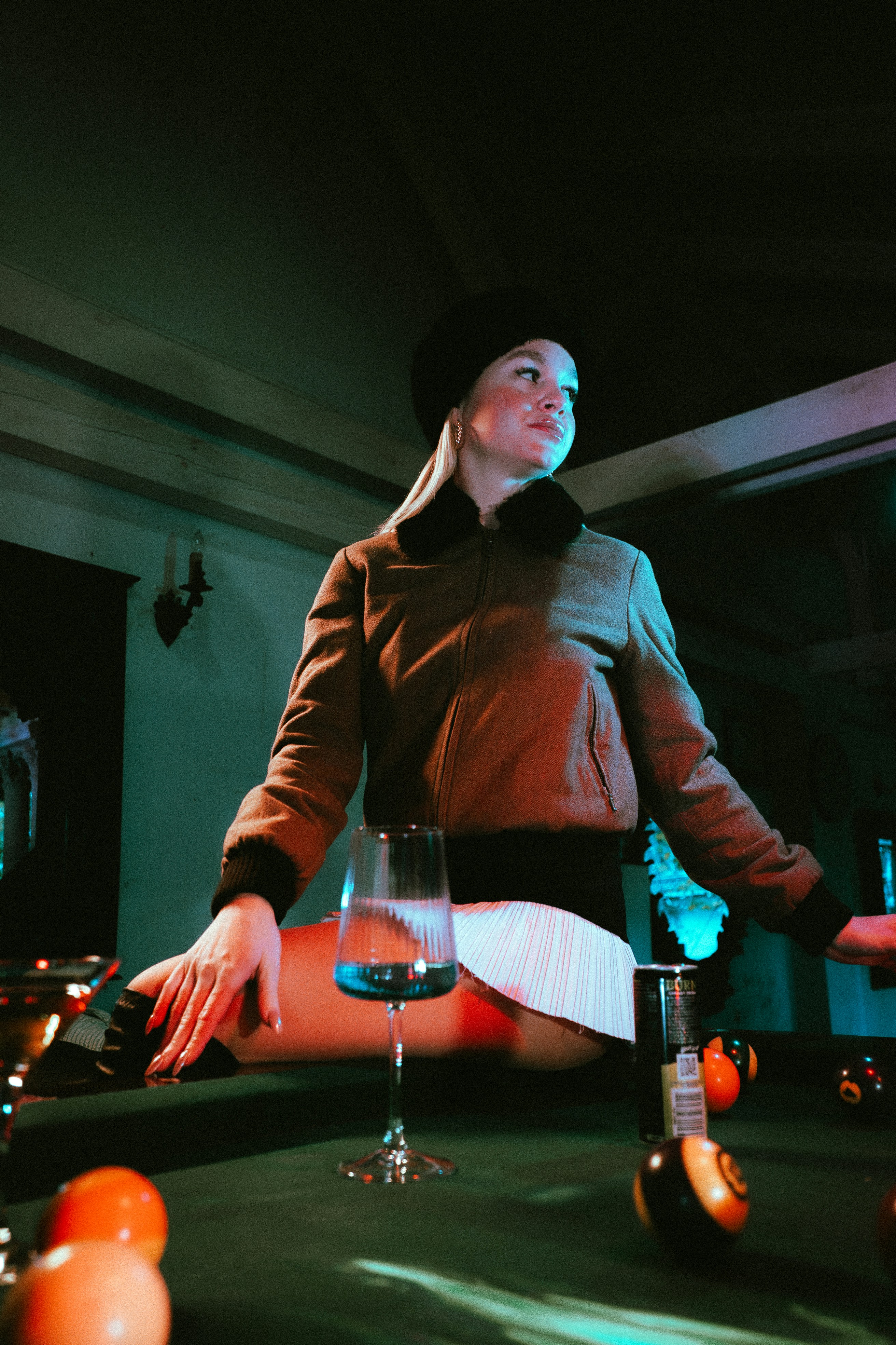 Woman in jacket and beret sits on a pool table.