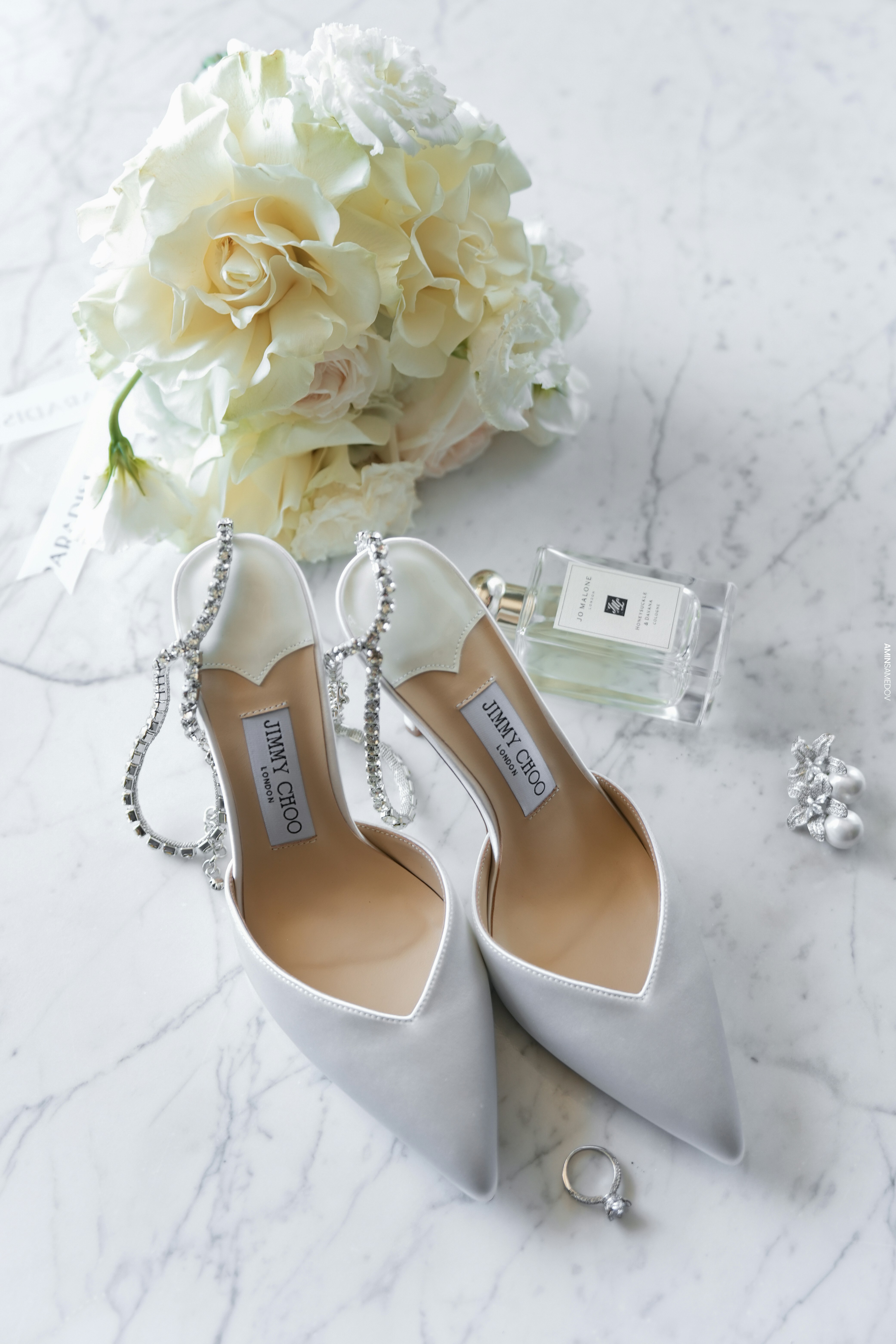 Elegante weiße Hochzeitsschuhe mit Blumenstrauß und Parfüm.