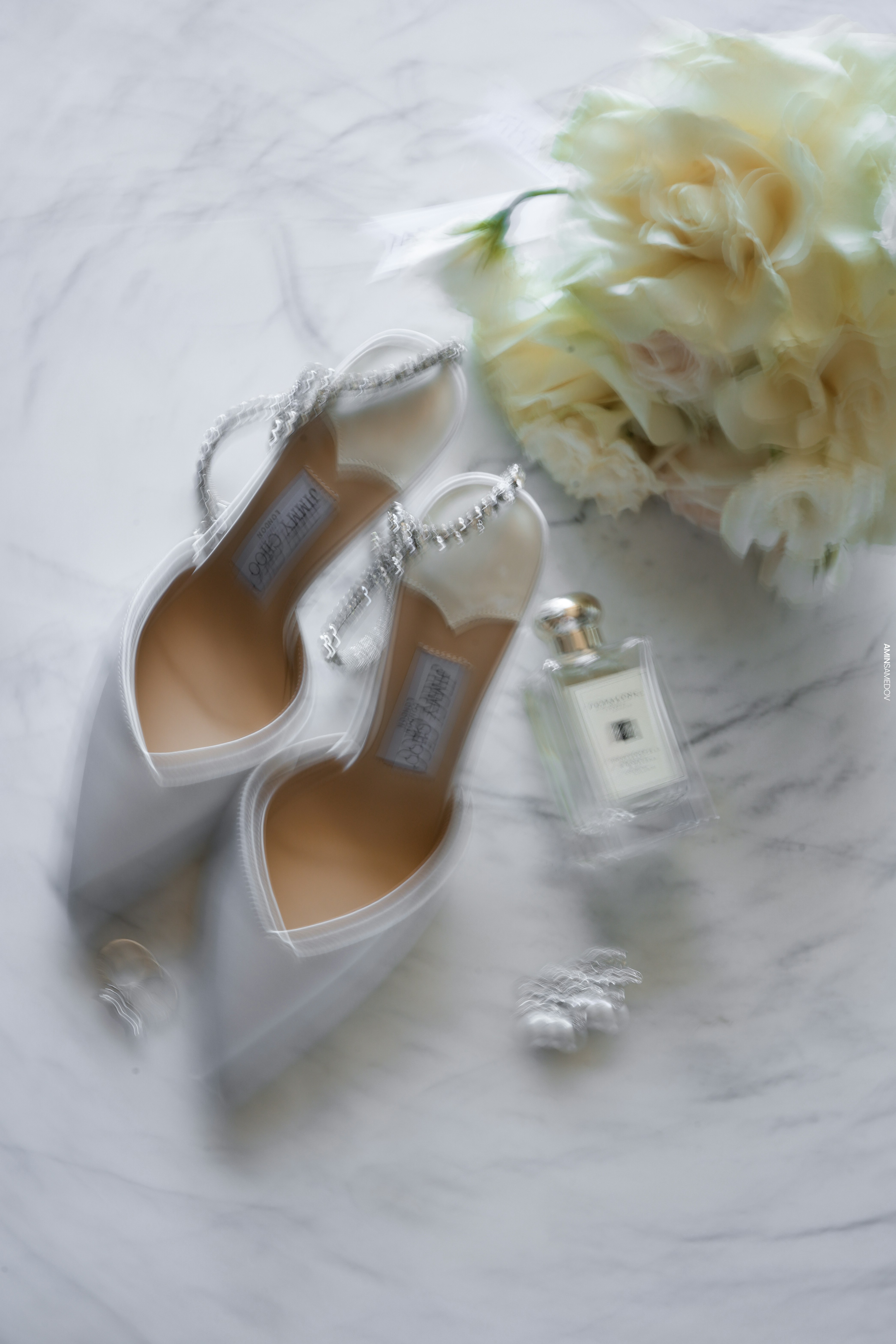 Elegant white heels, perfume, and flowers on marble