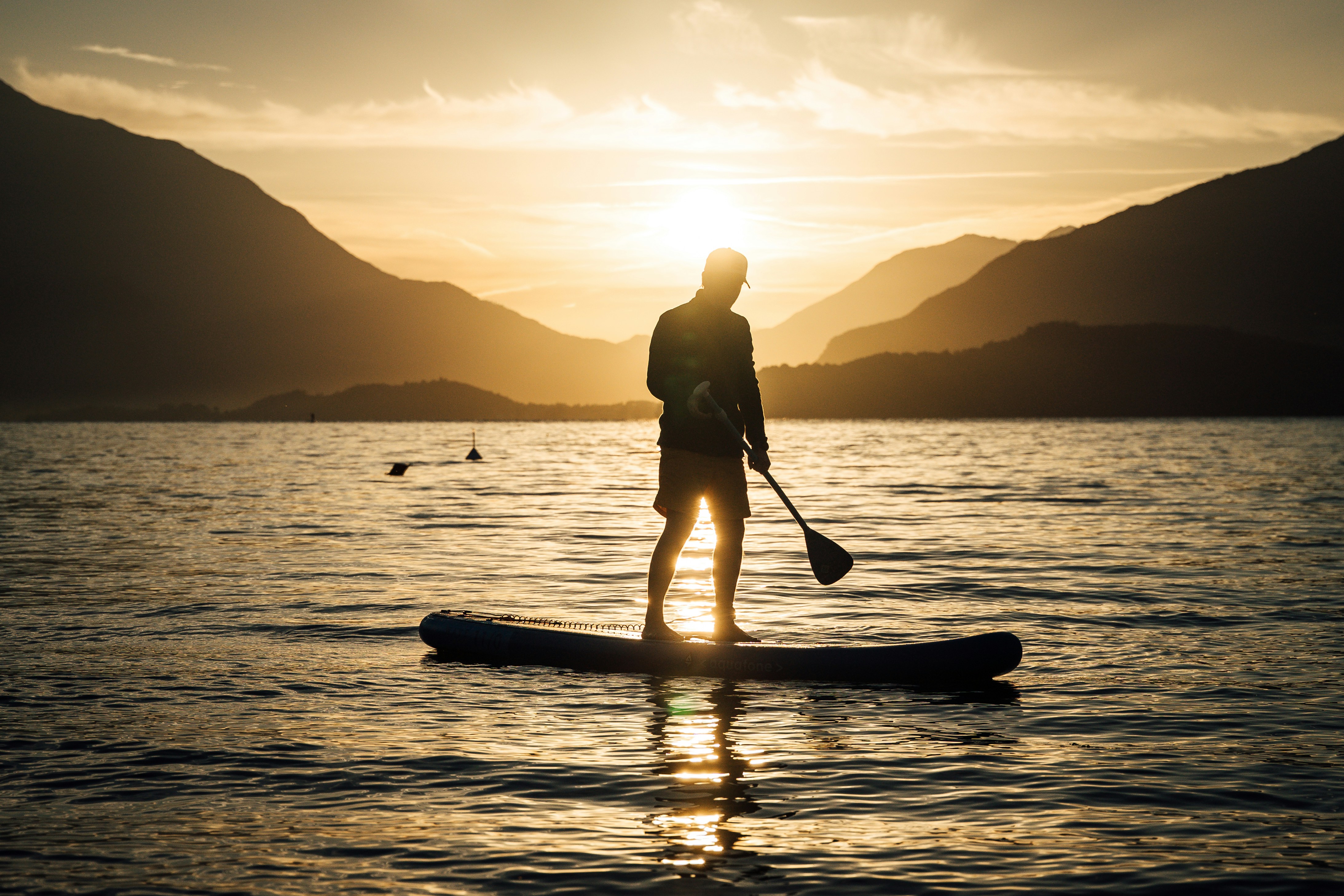 Person paddleboarding on a lake at sunset.