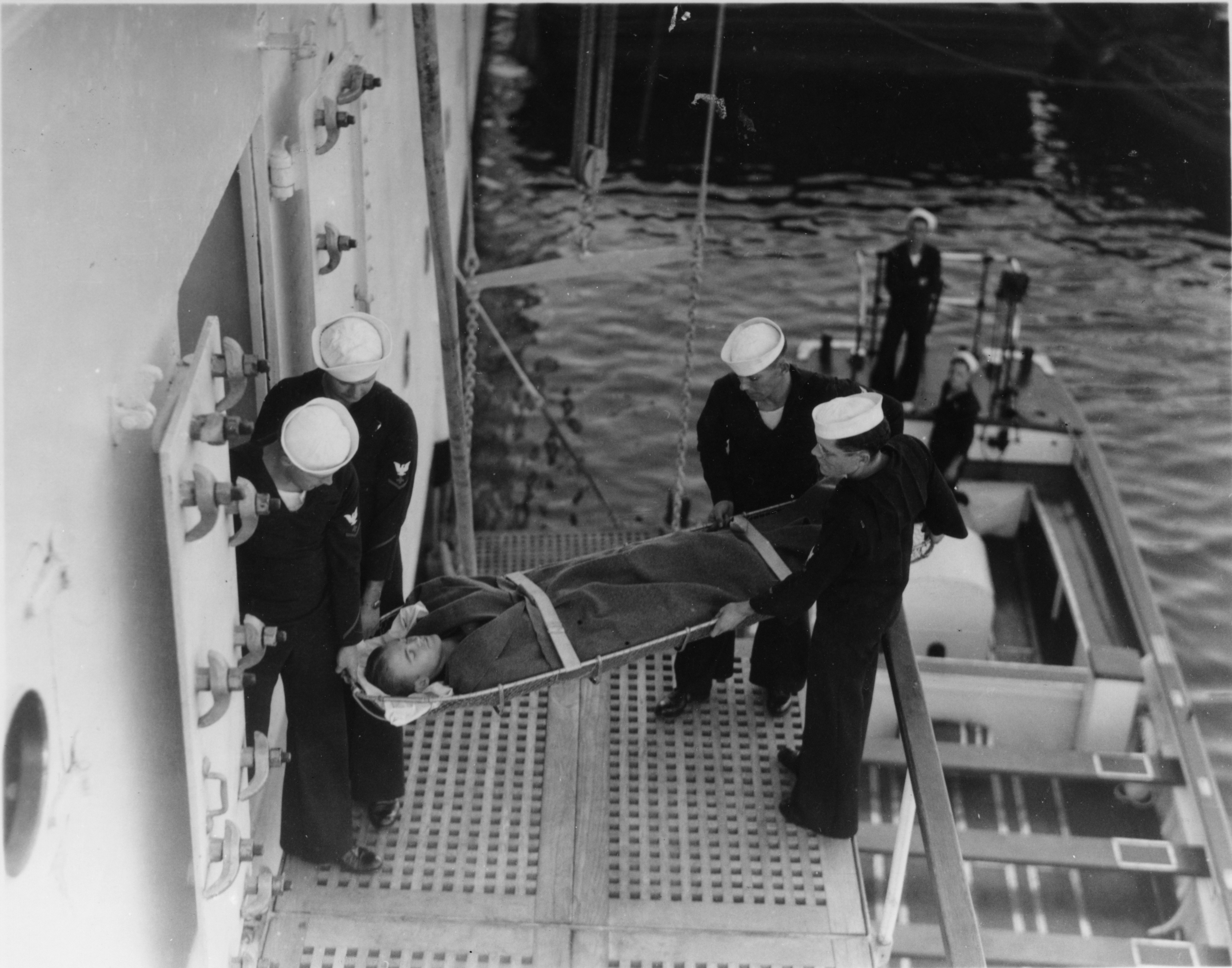 Sailors carry injured person on a stretcher from ship