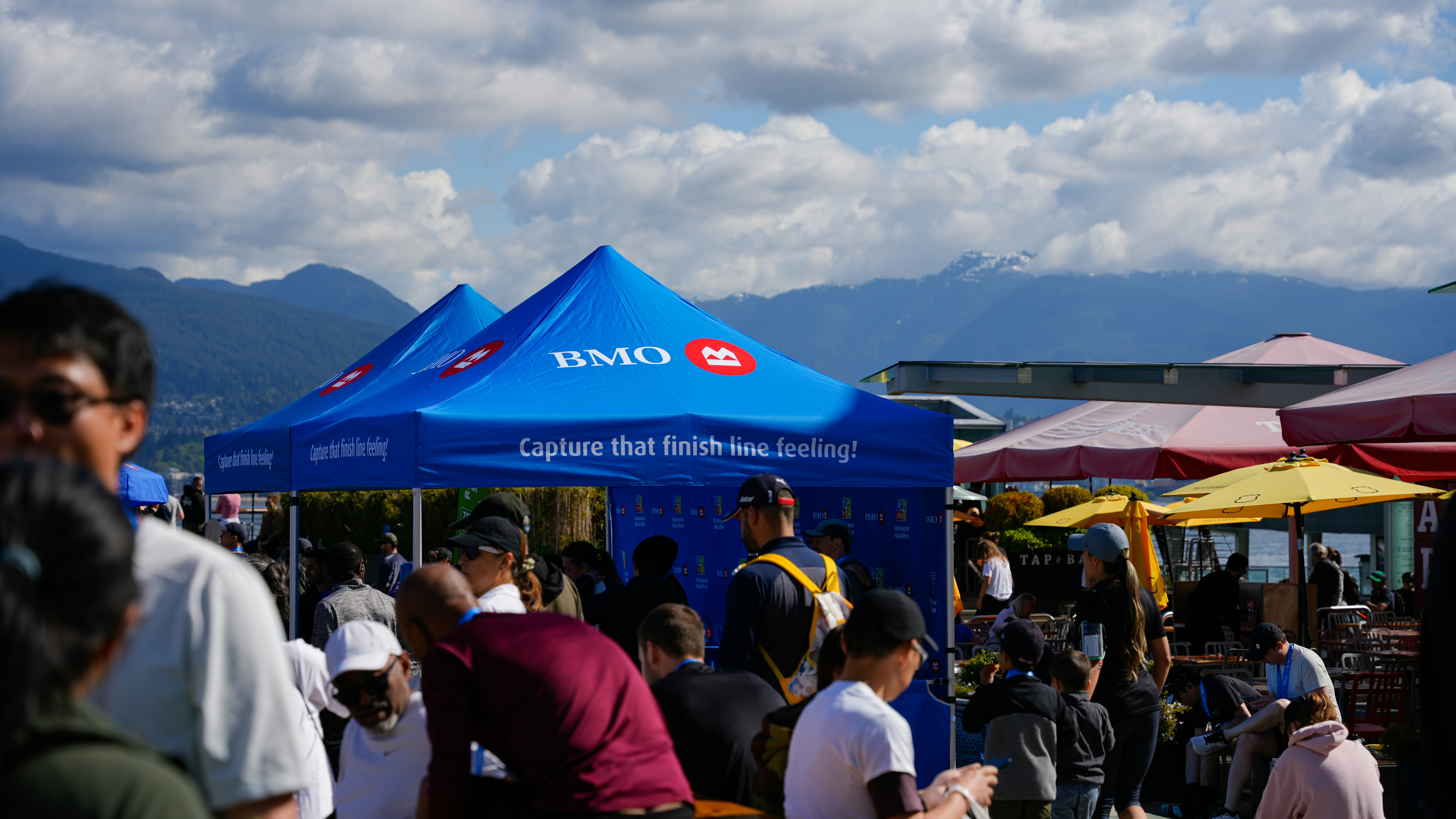 People gathered under blue tents with mountains in background