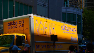 Yellow delivery truck with alkiss water branding.