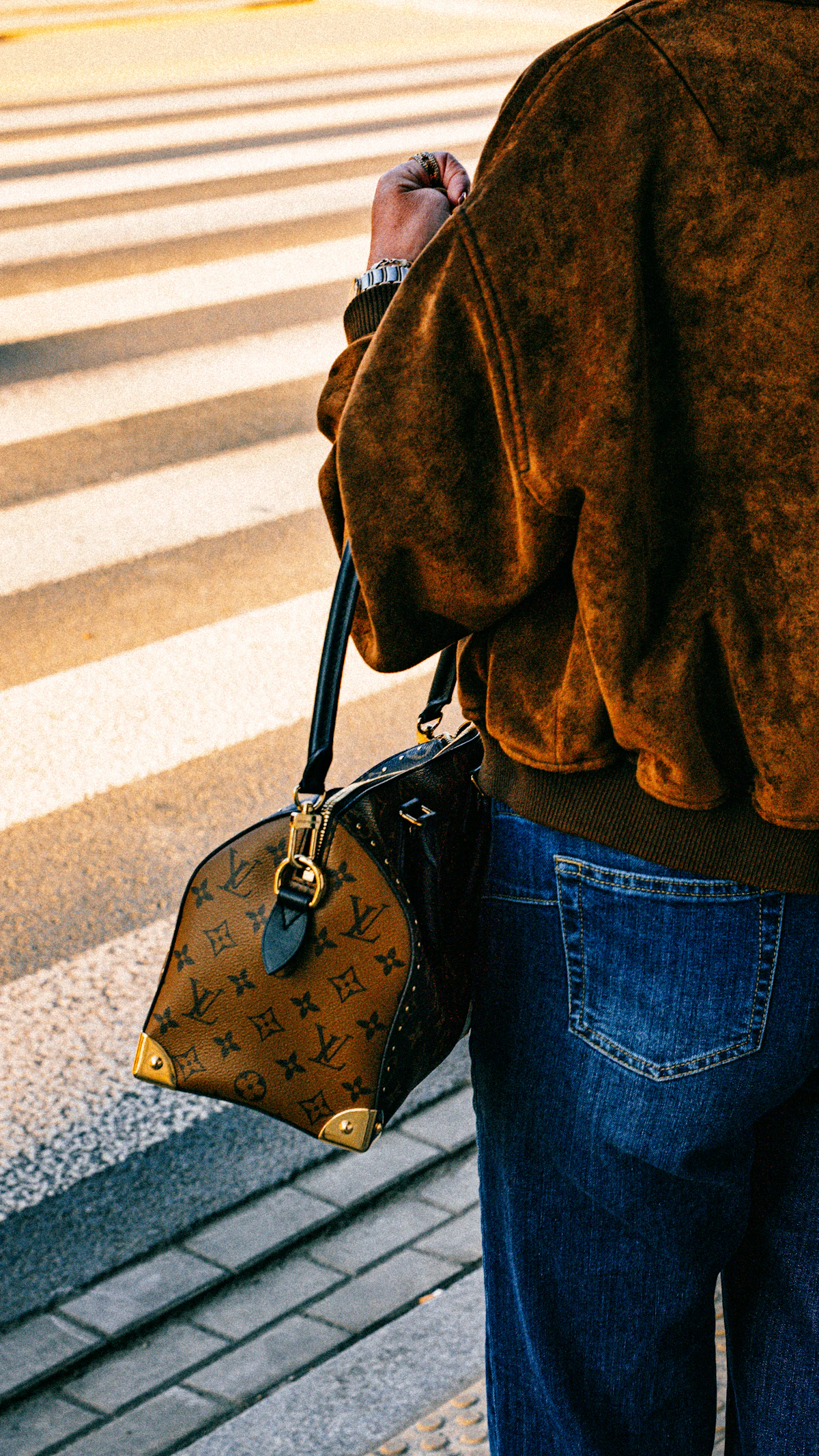 Person carrying a crossbody handbag across a city crosswalk
