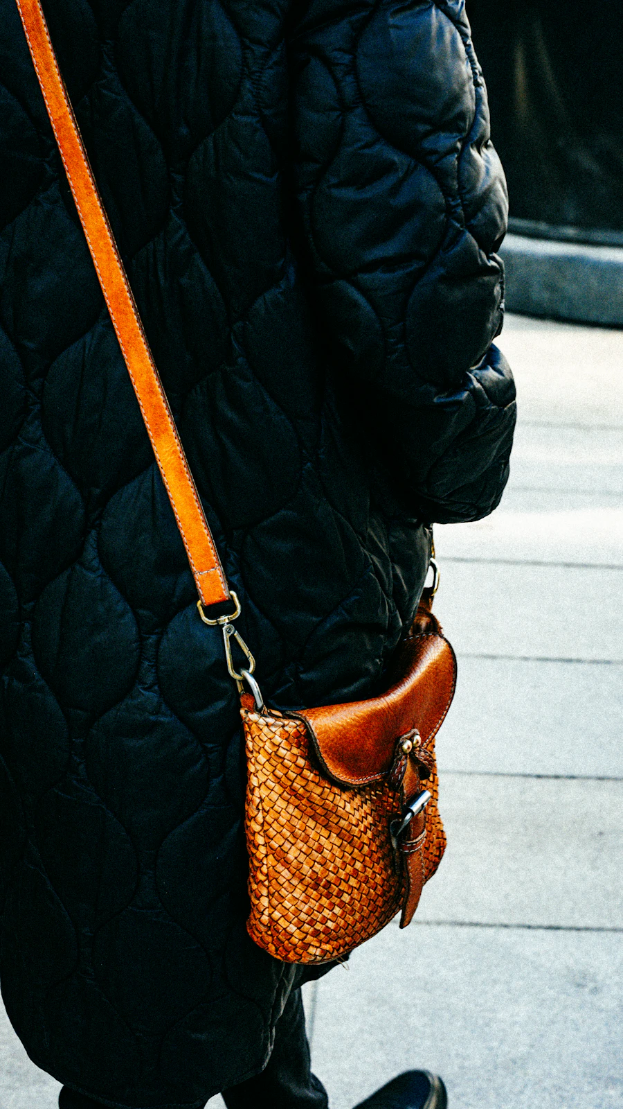 Woven leather crossbody bag worn with a dark coat