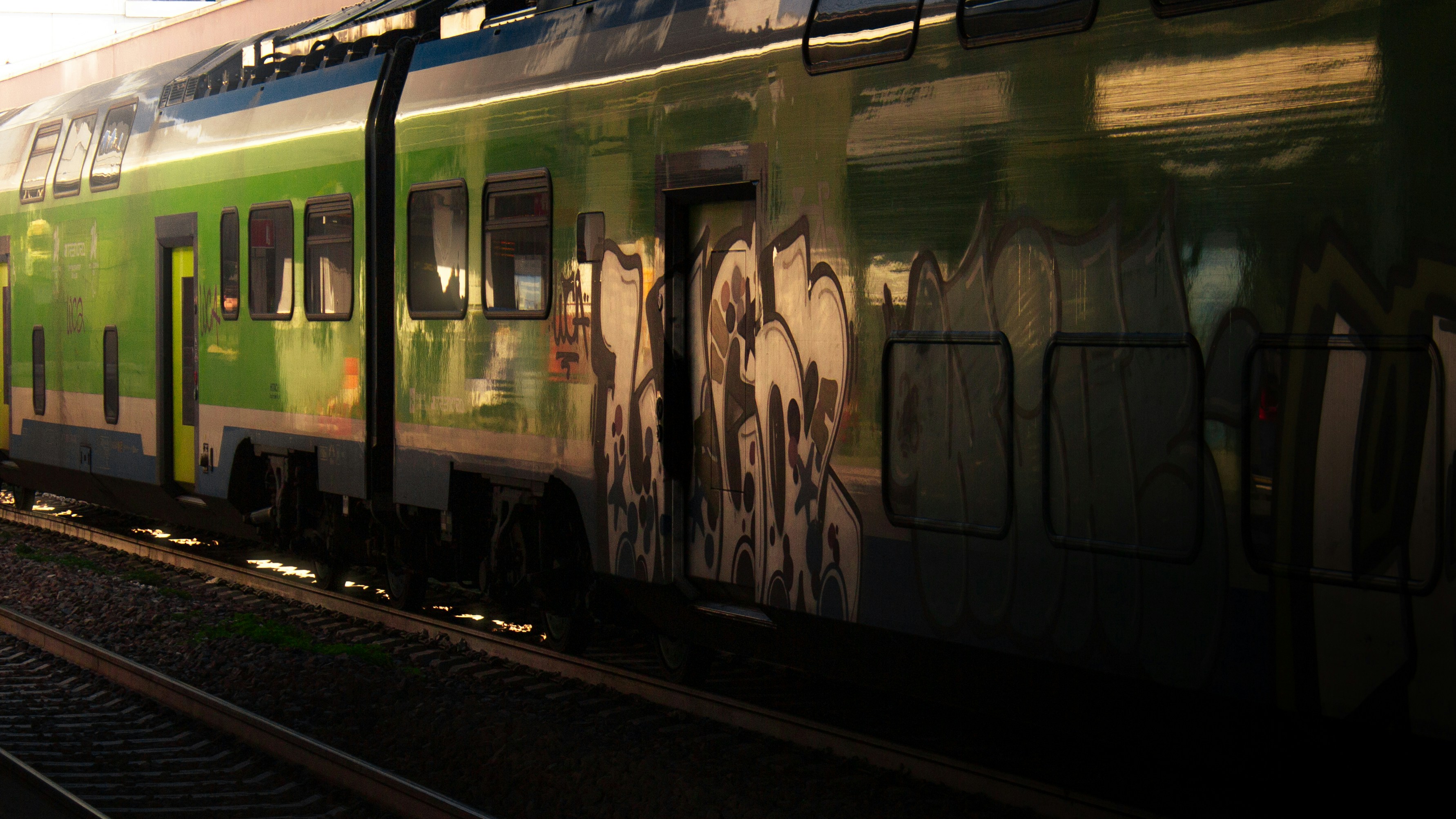 Green train car covered in graffiti on tracks