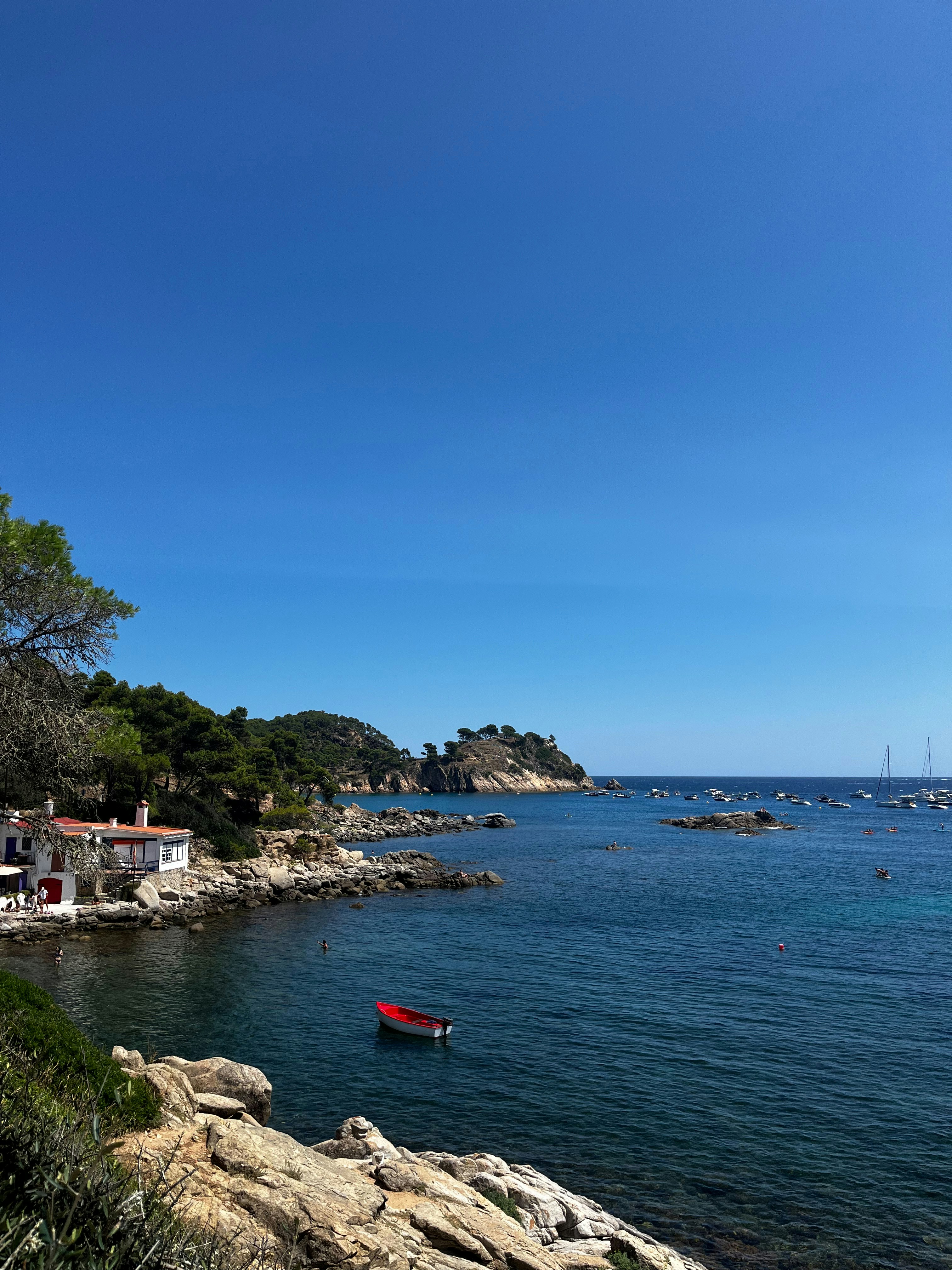 Un barco rojo flota en aguas azules cerca de la costa rocosa.