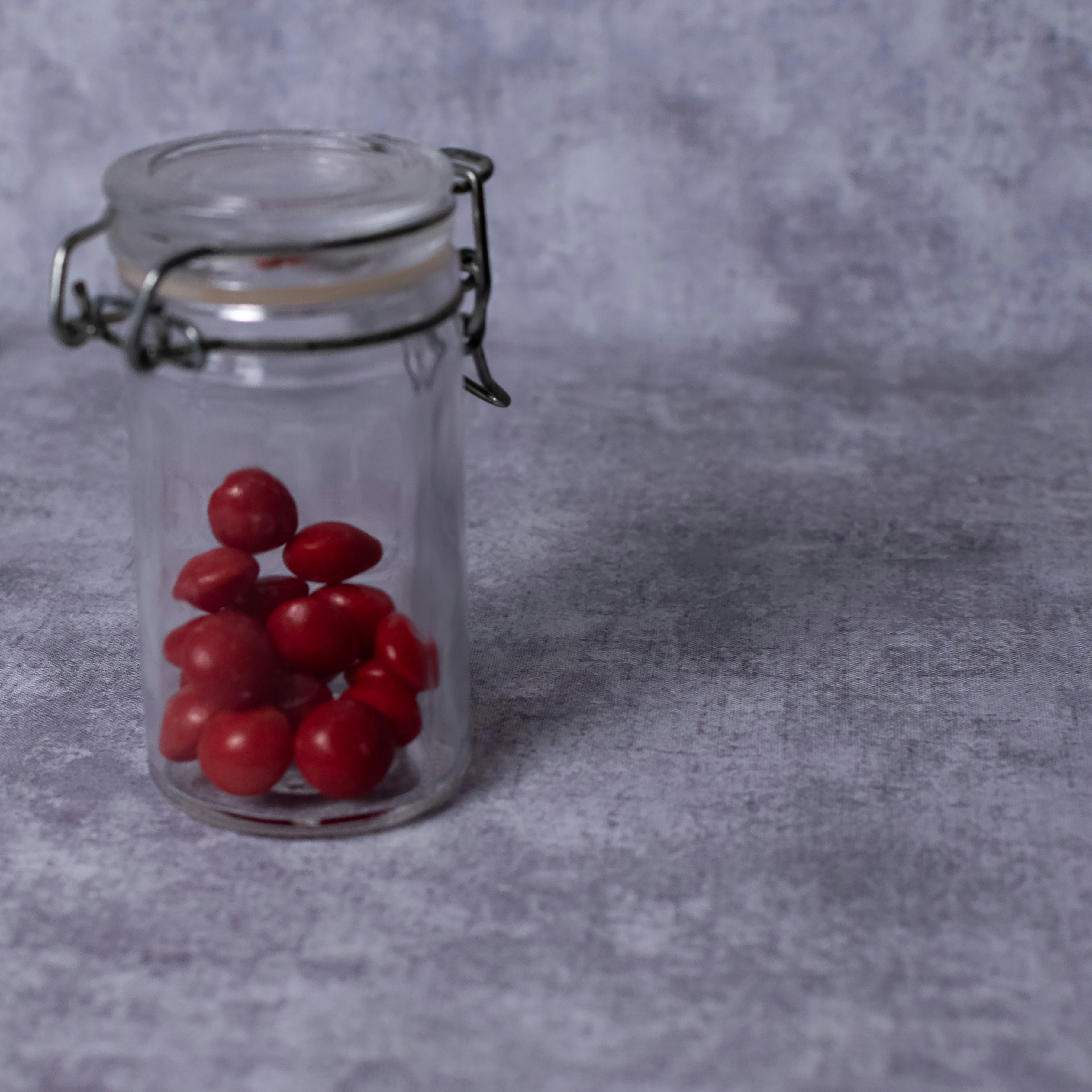 Glass jar filled with red candies on a textured surface.