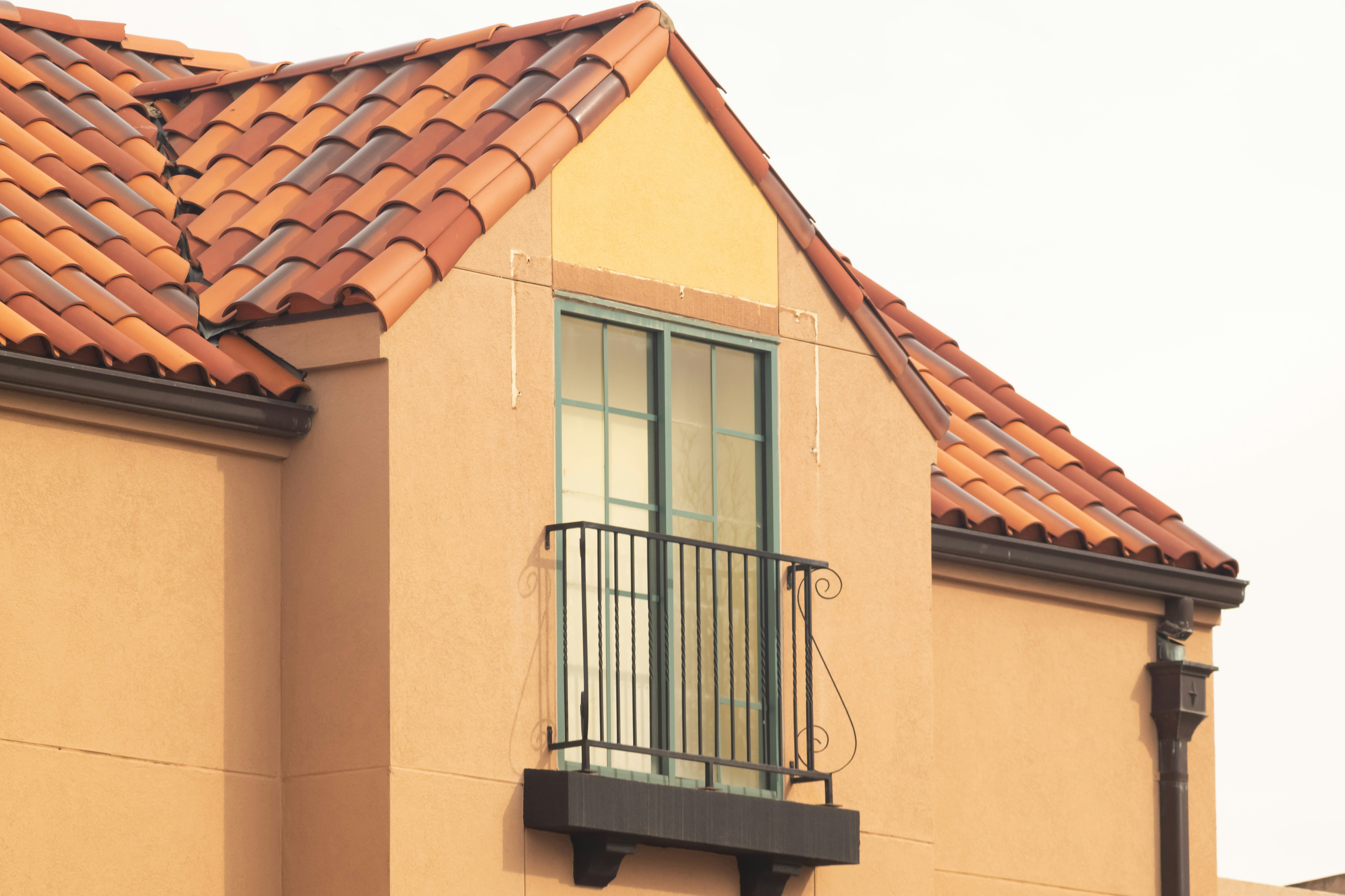 Orange stucco building with red tile roof and balcony.