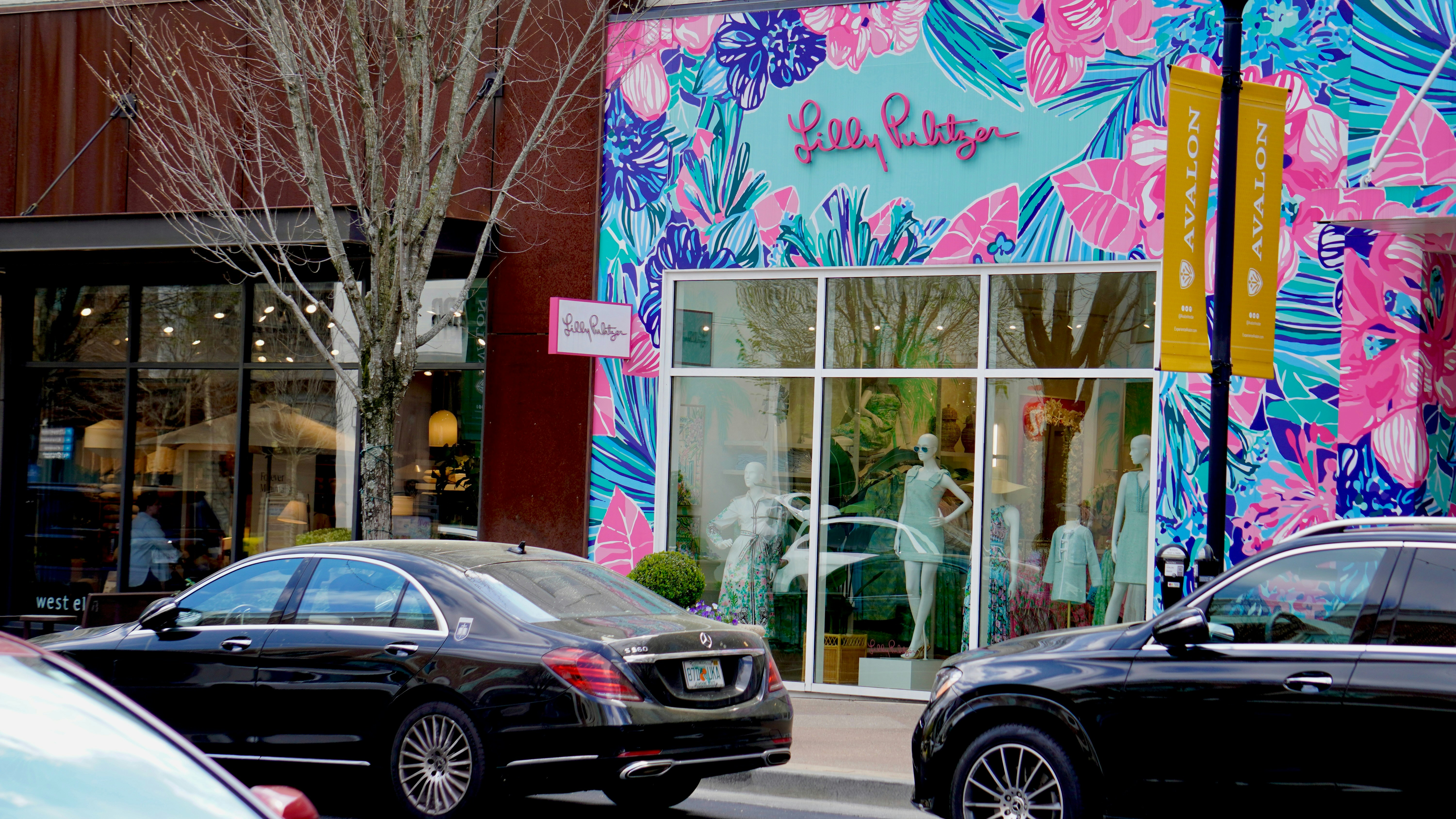 Colorful storefront with mannequins and parked cars.