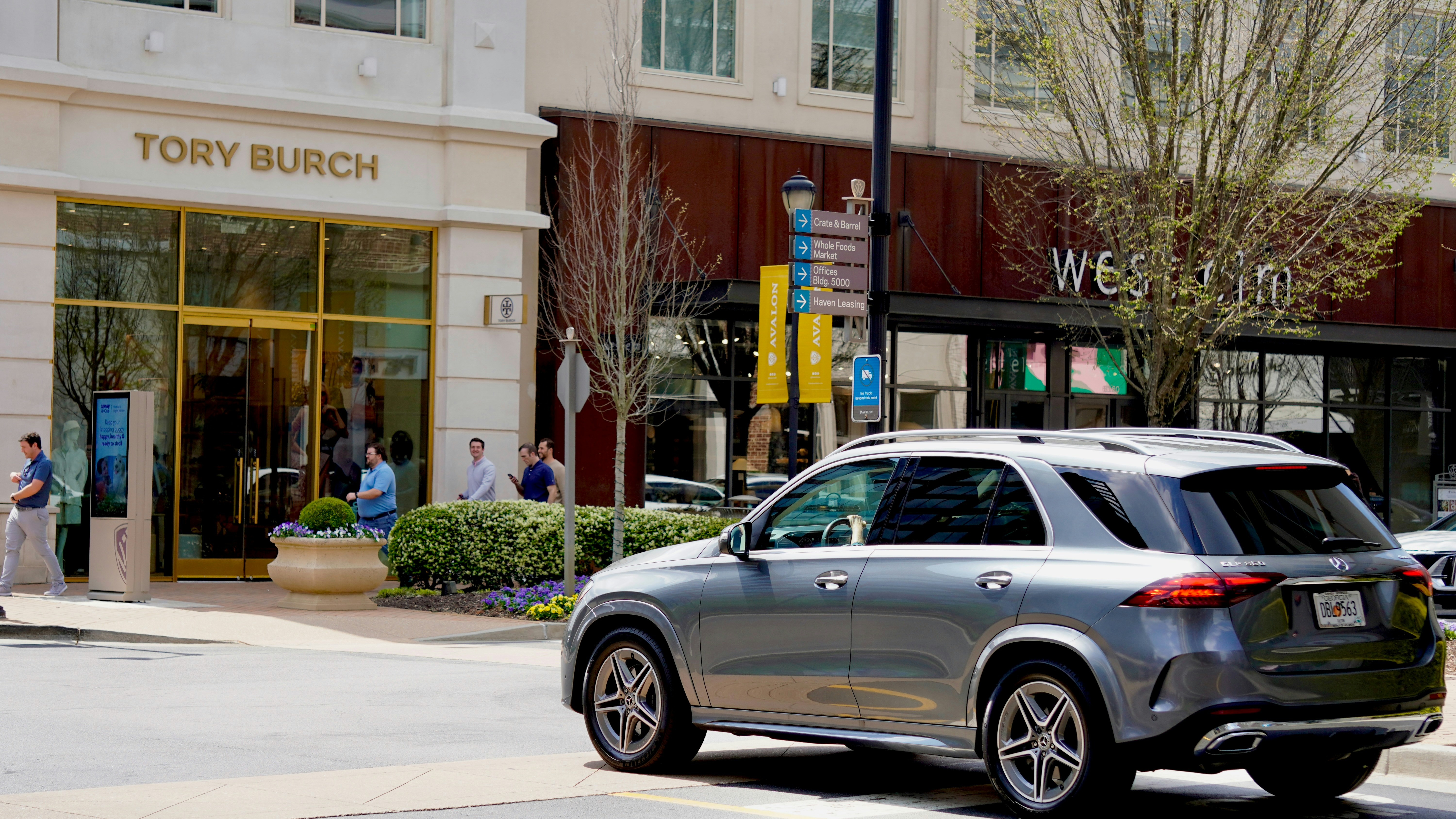 A grey suv drives past a tory burch store.