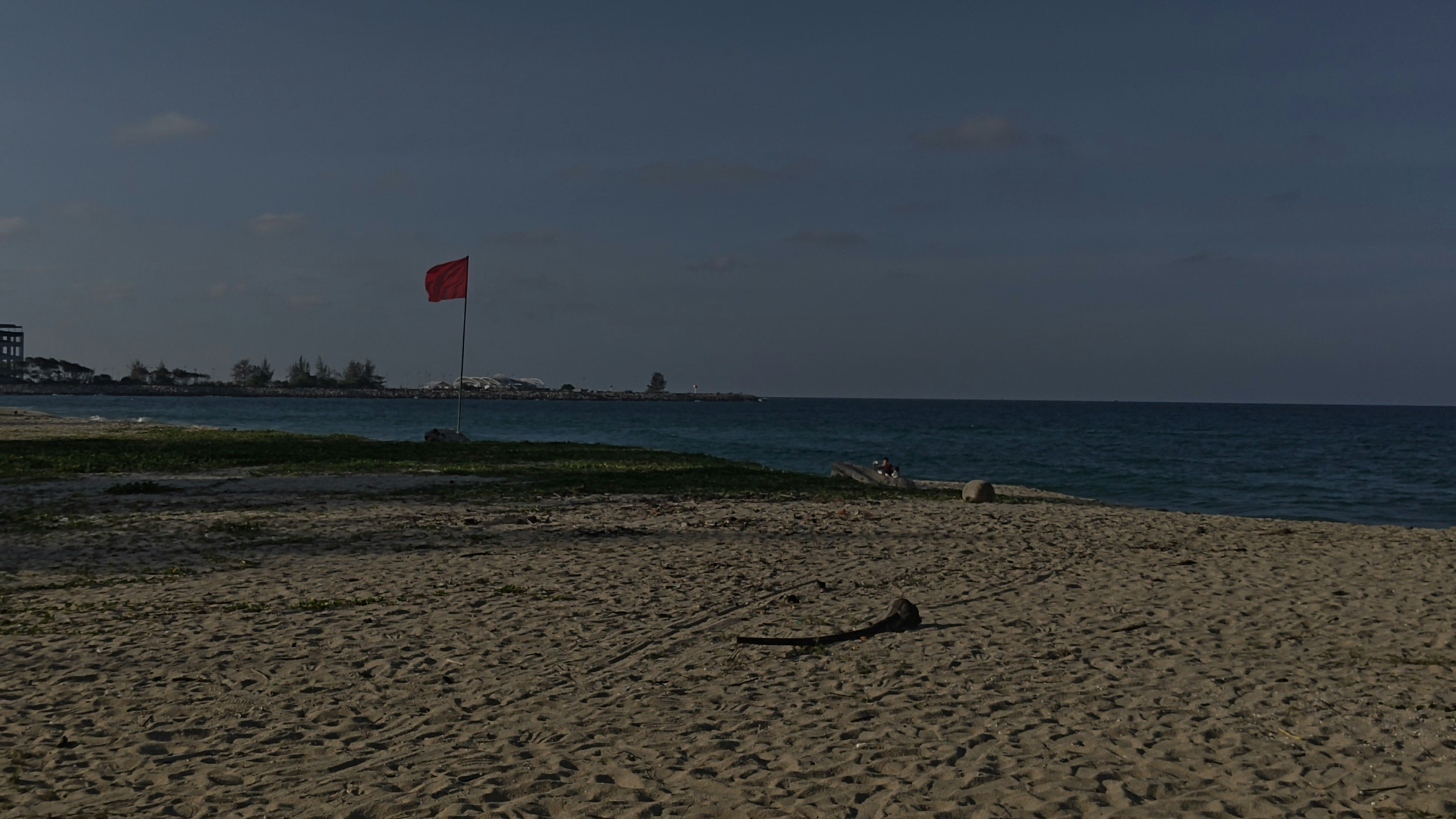 Red flag on a sandy beach by the blue ocean