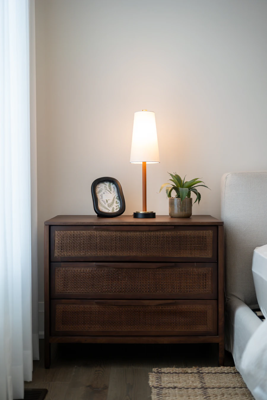 Mesa de noche de madera oscura con frentes de caña, lámpara y planta