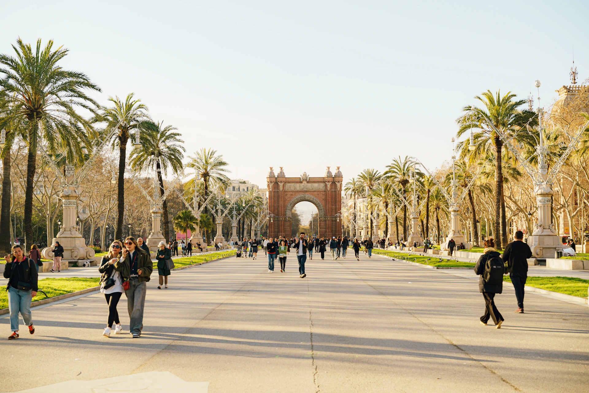 People walking down a tree-lined avenue towards an arch.