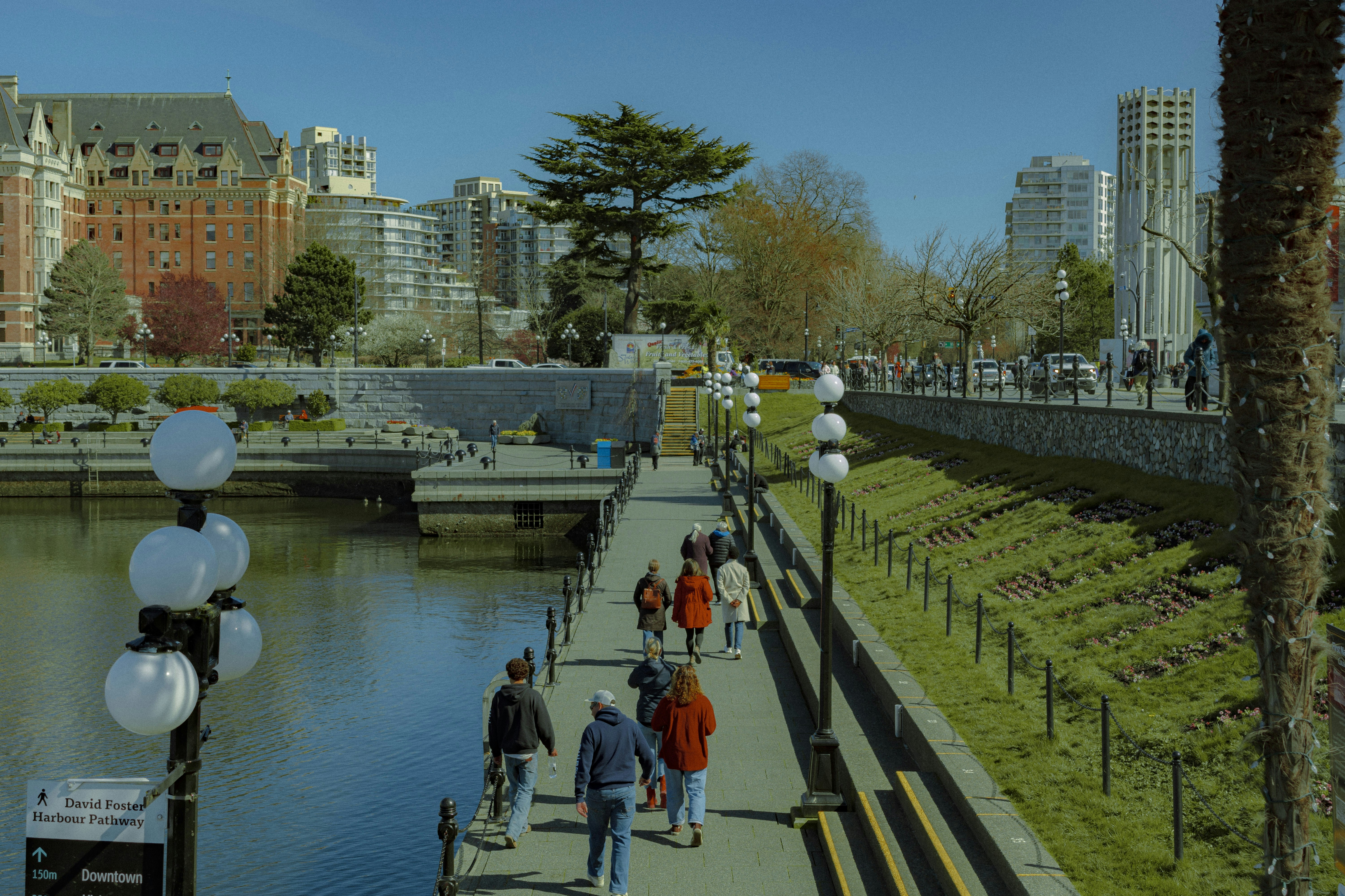People walk along a waterfront path with buildings in background.