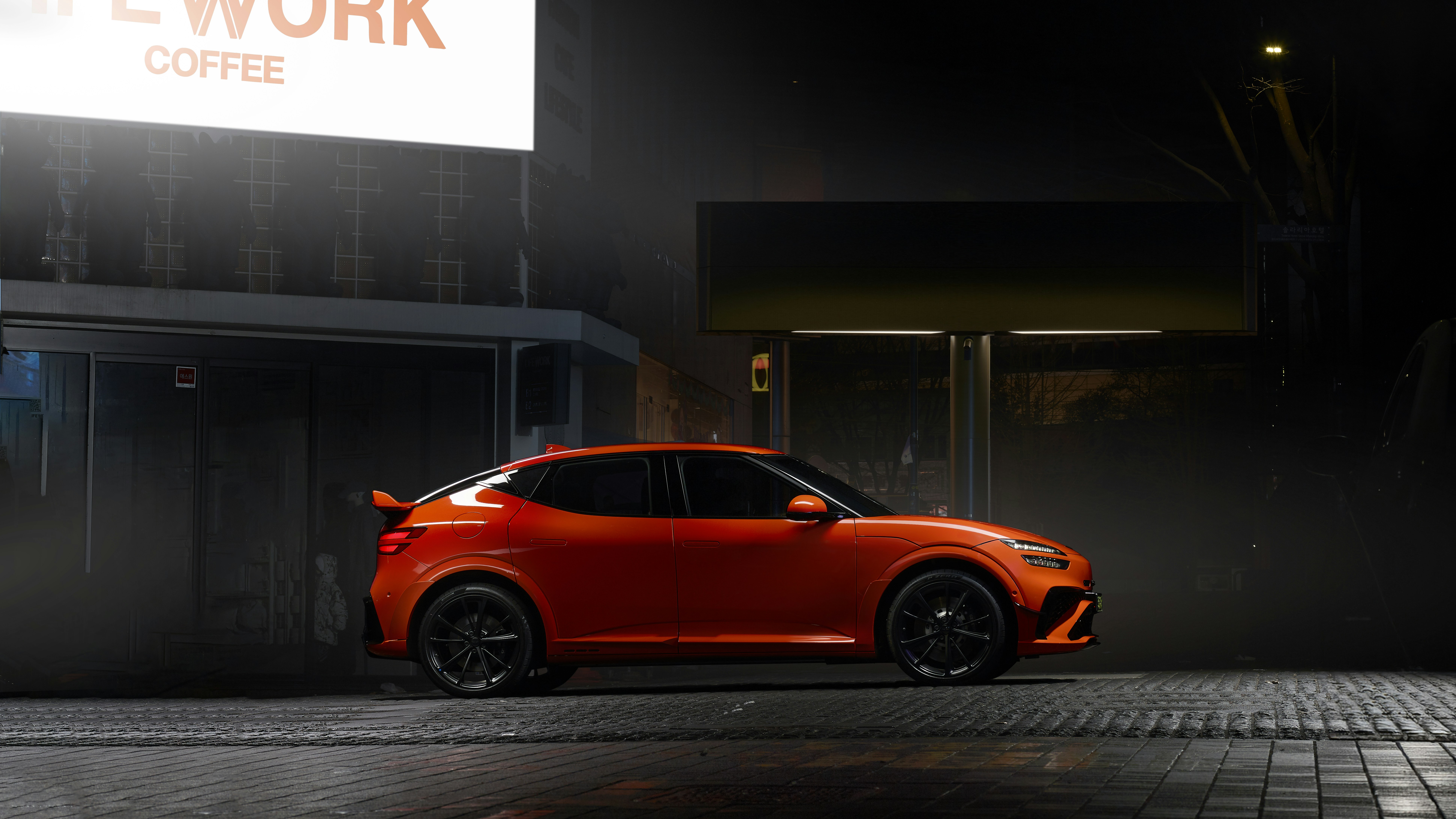 Orange sports car parked on wet city street at night