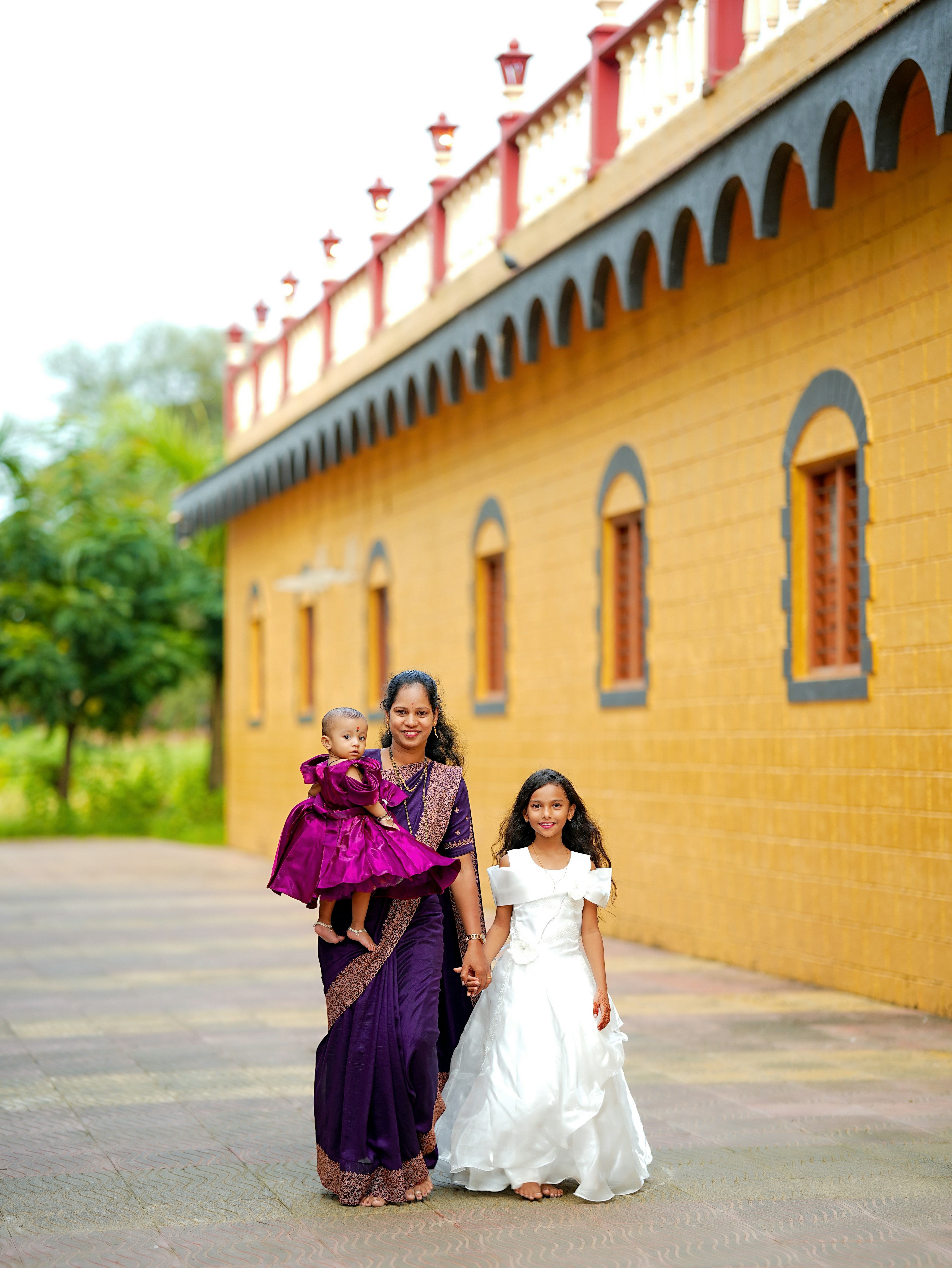 Mother and two daughters in dresses walk outside.