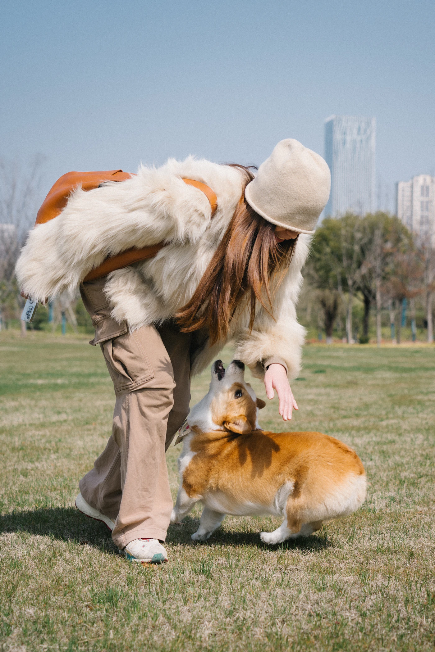 Woman interacting with a corgi during outdoor play in a park