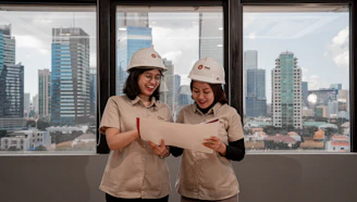Two women in hard hats review blueprints indoors.