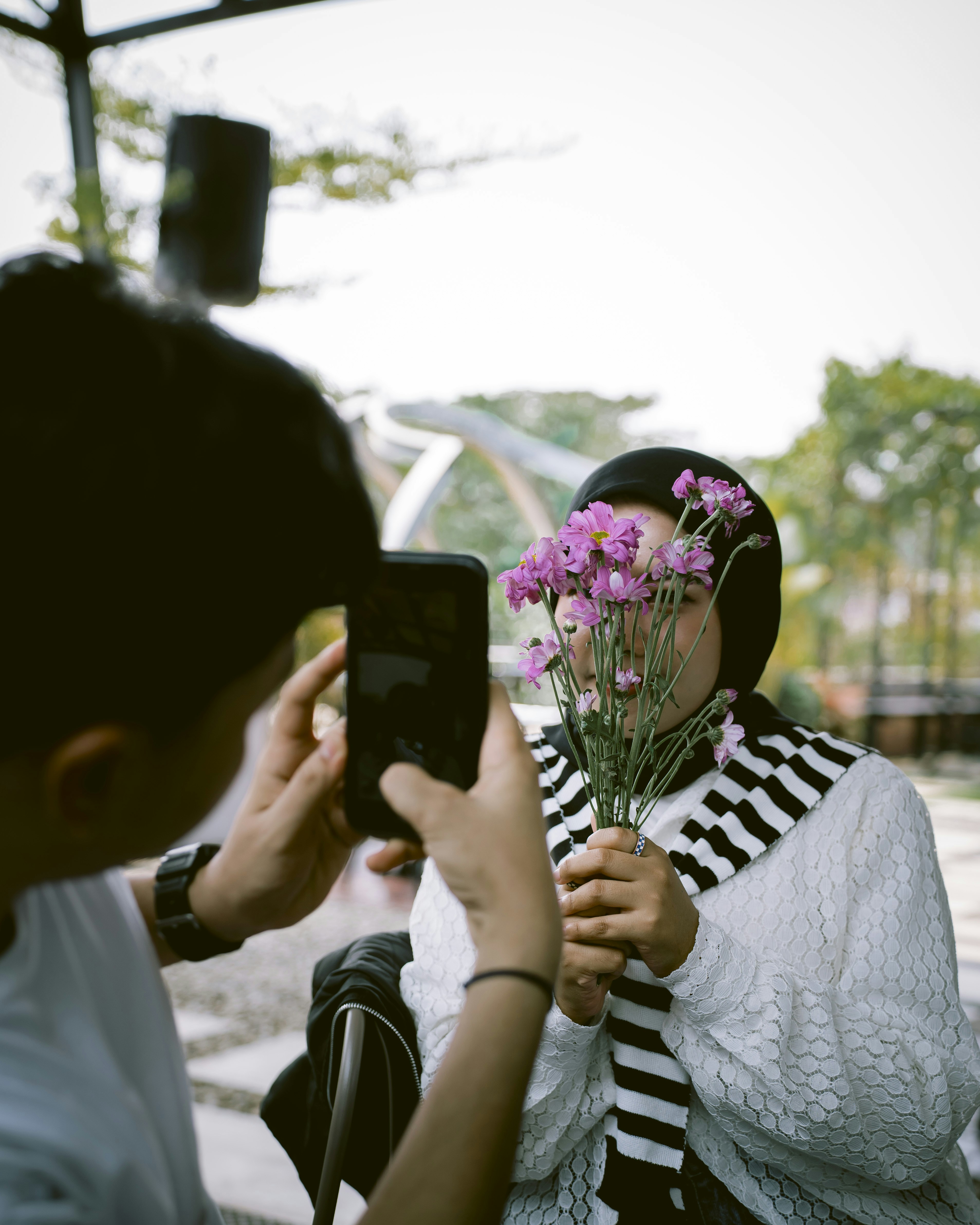 Woman in hijab holding pink flowers while being photographed