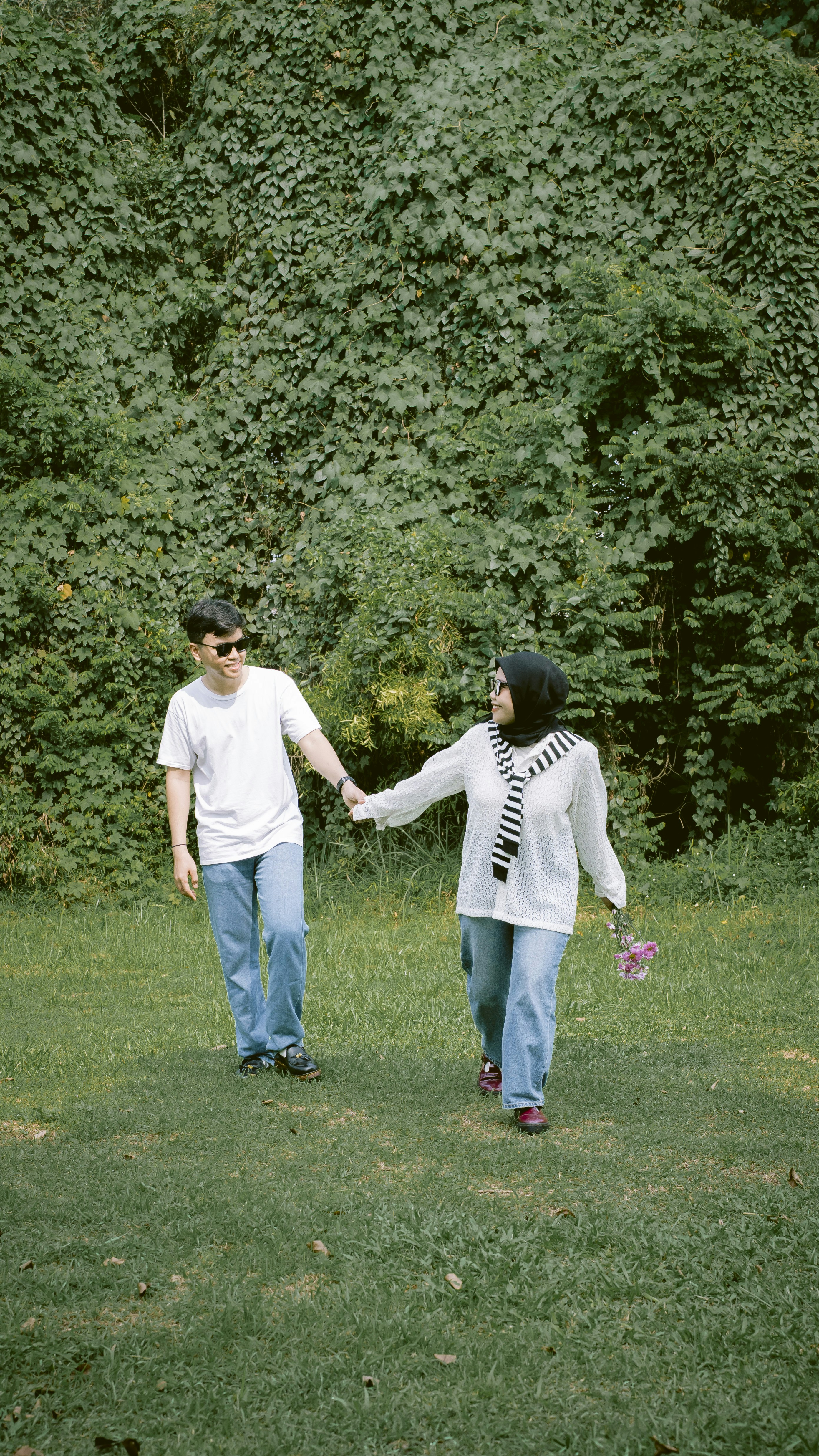 A couple walks hand-in-hand in a grassy park.