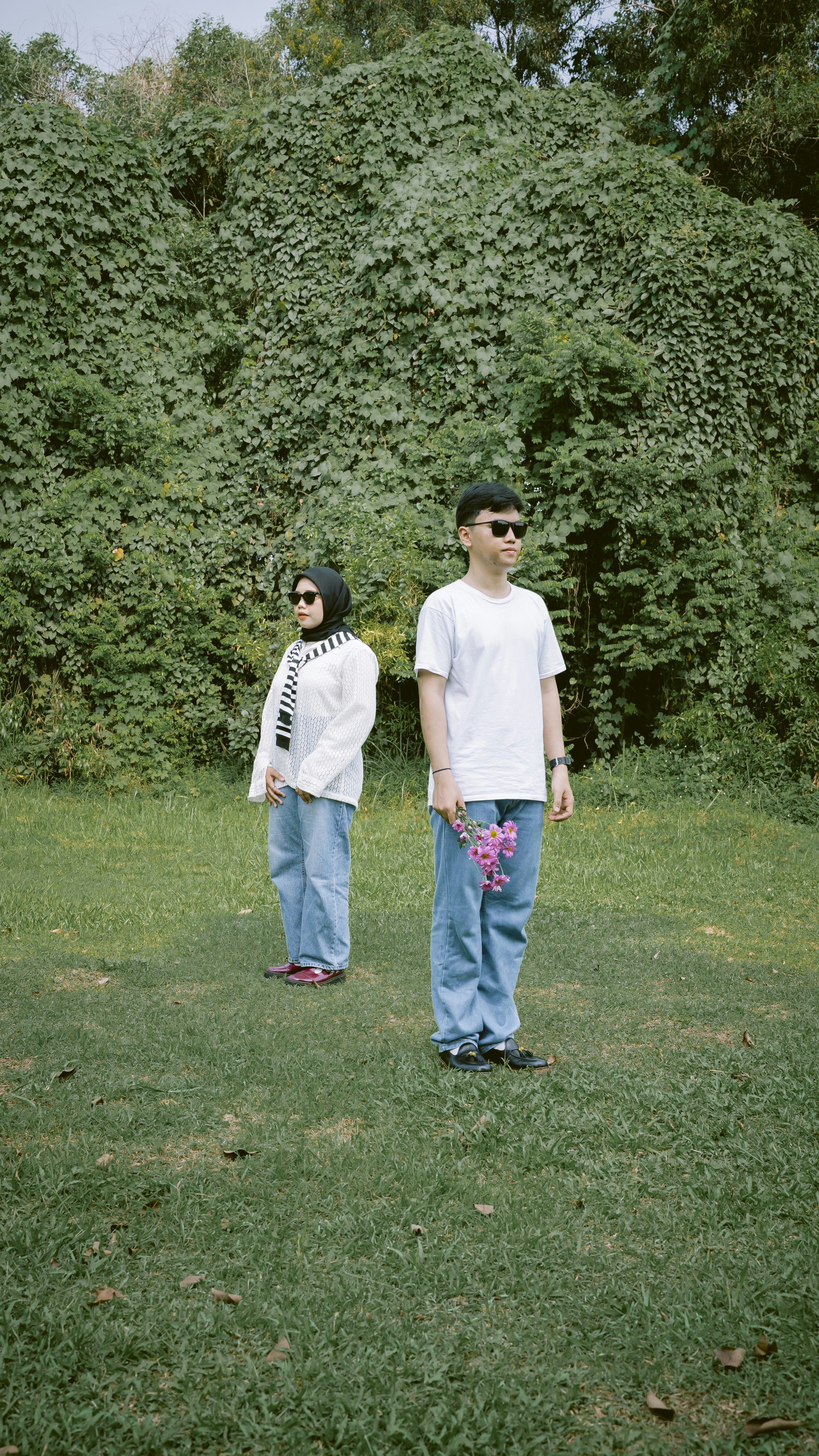 Couple standing in a grassy field with lush green foliage